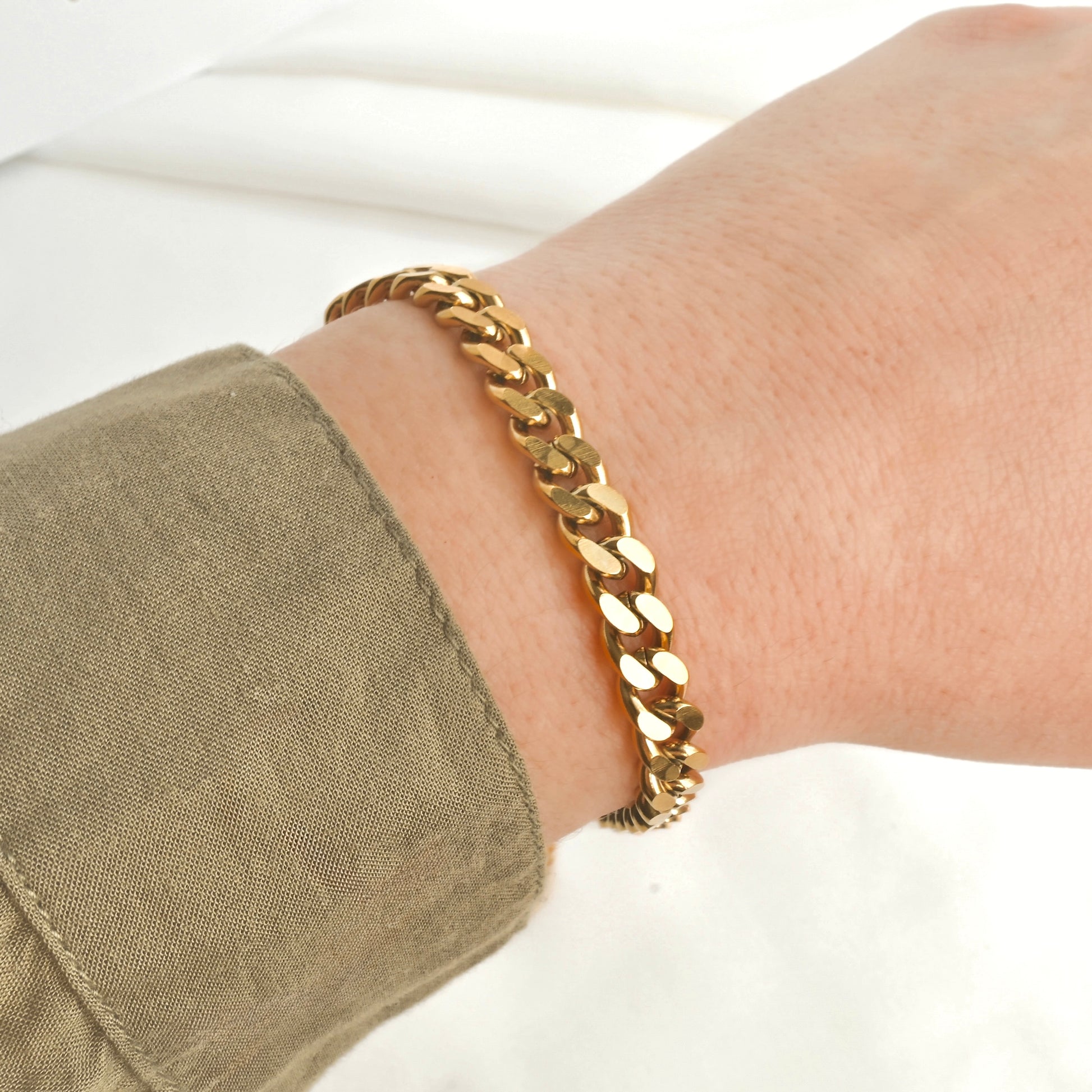 Chunky gold cuban chain bracelet on a wrist with a khaki shirt
