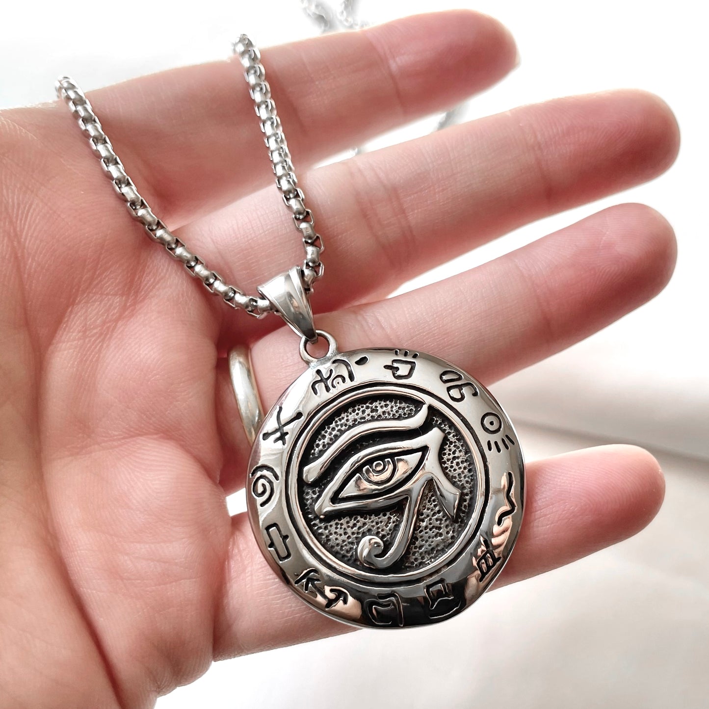 Antiqued silver eye medallion held in a hand against a blurred background