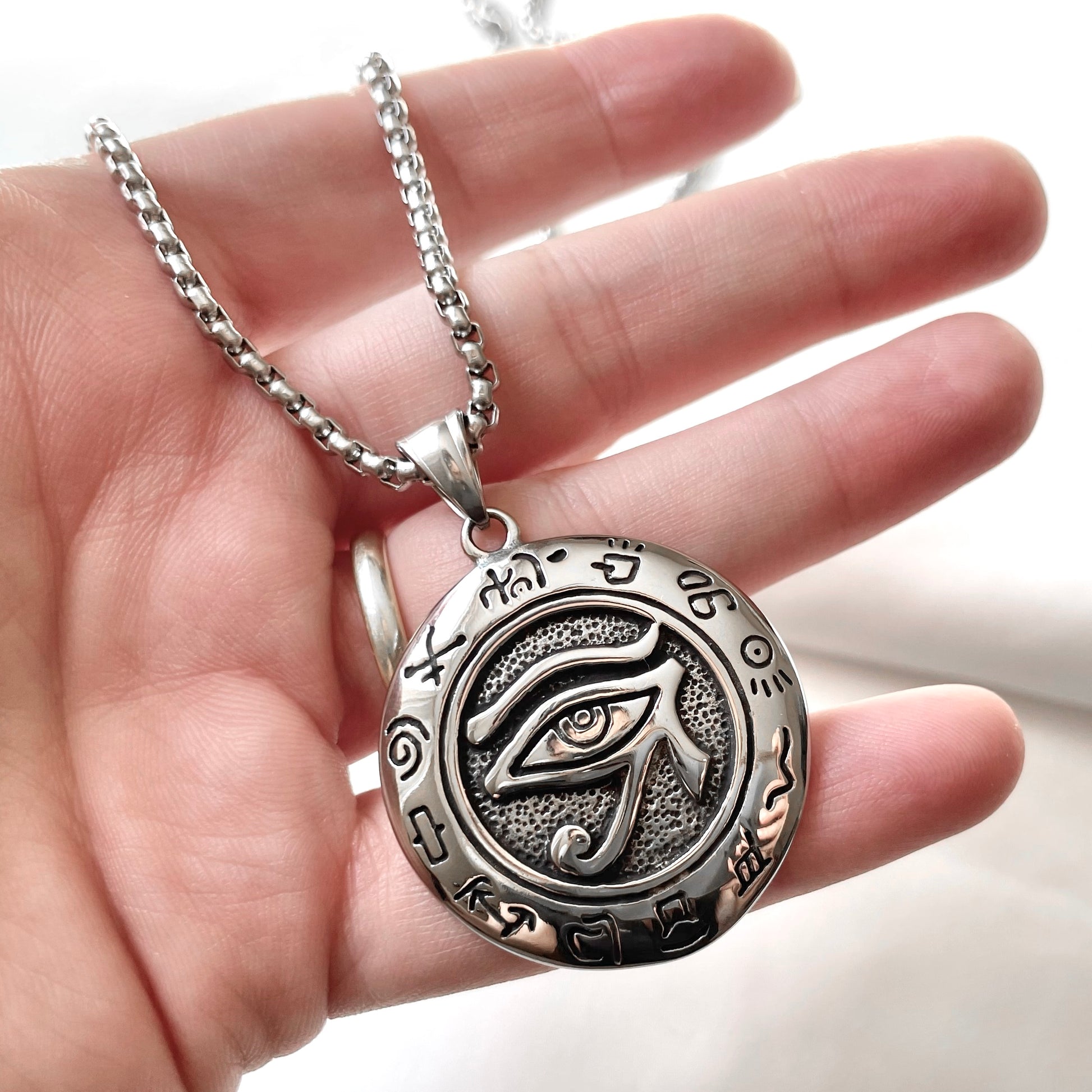 Antiqued silver eye medallion held in a hand against a blurred background