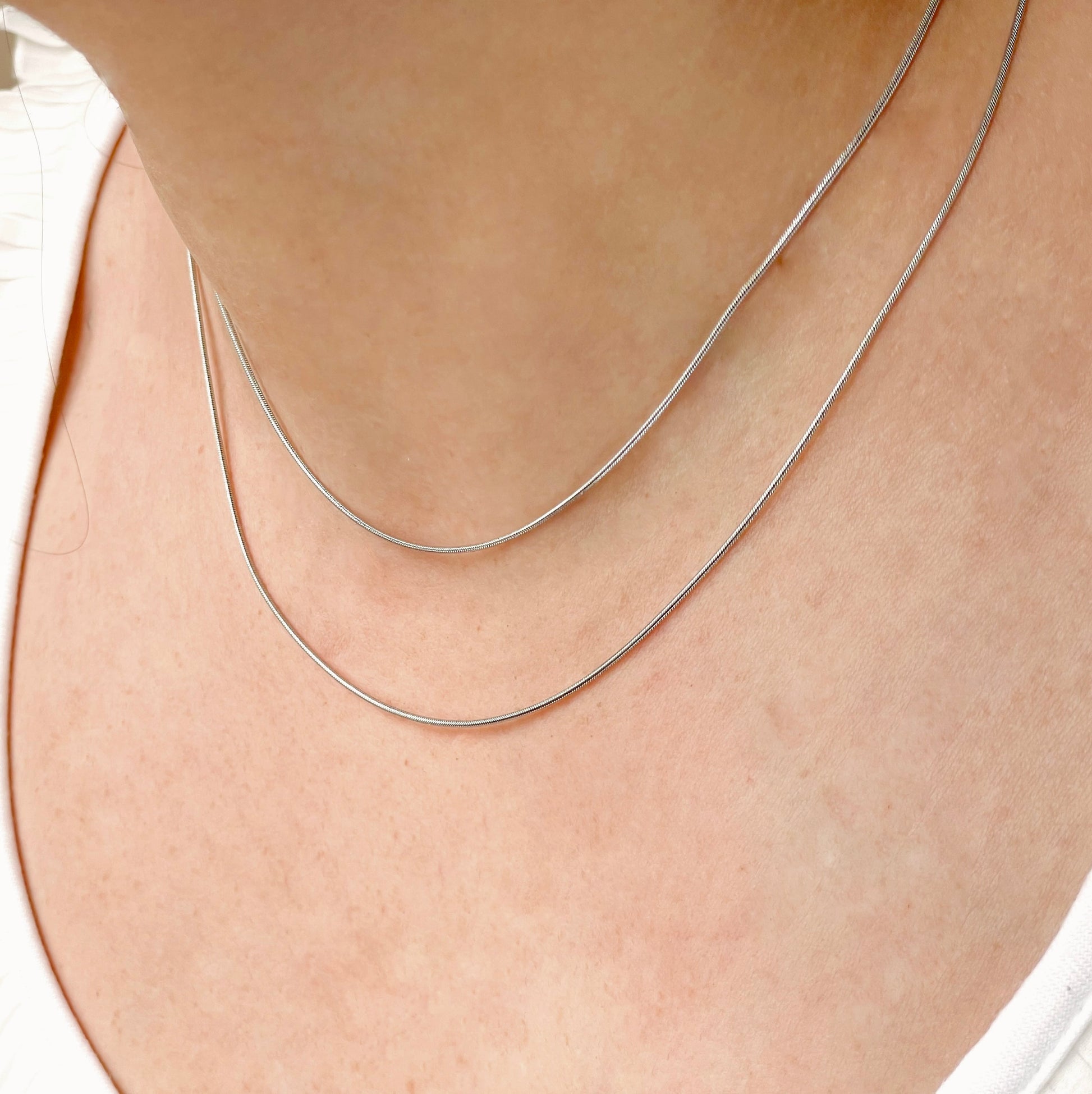 Silver necklace on a person's neck with a plain background