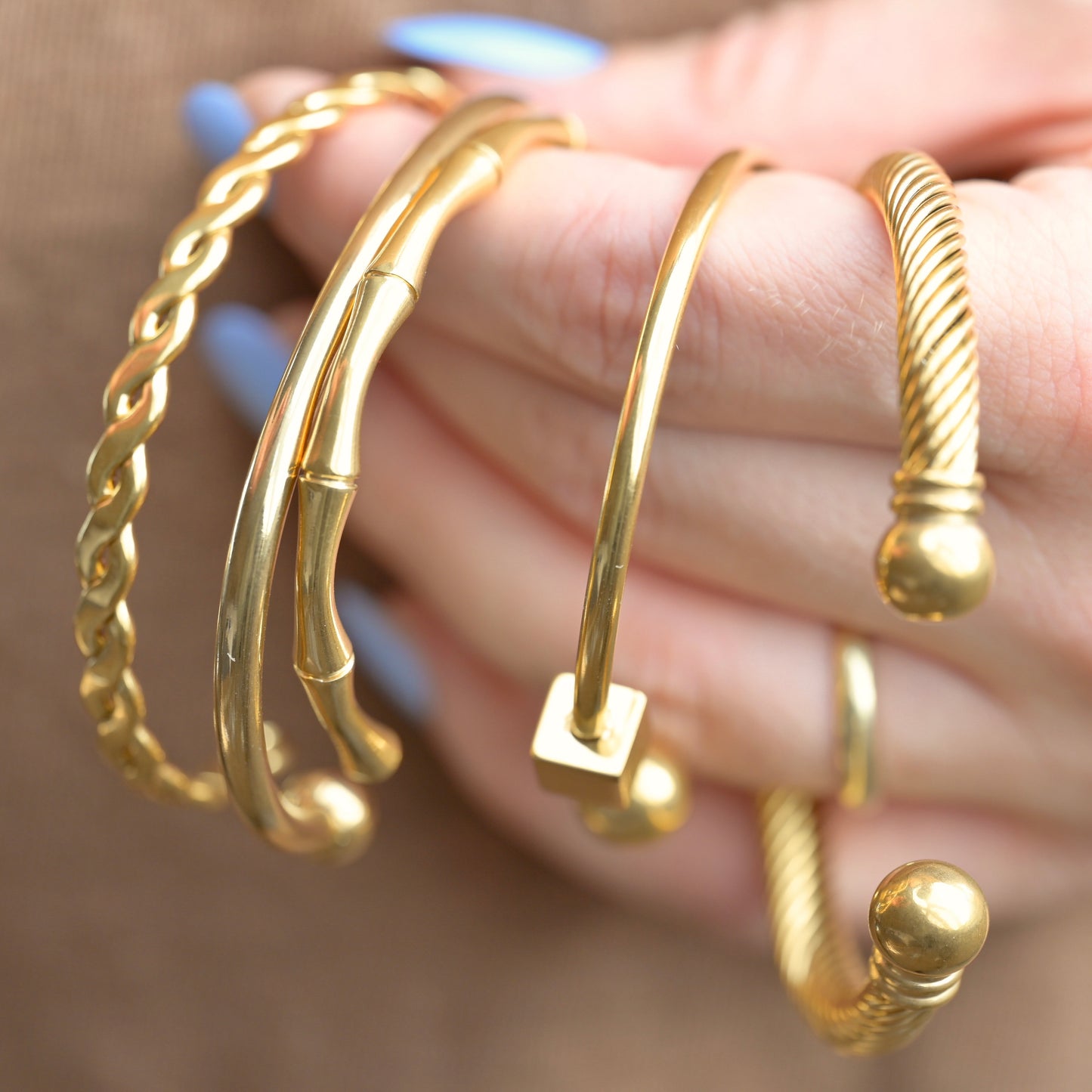 Gold cuff bracelets on a hand with a blurred background