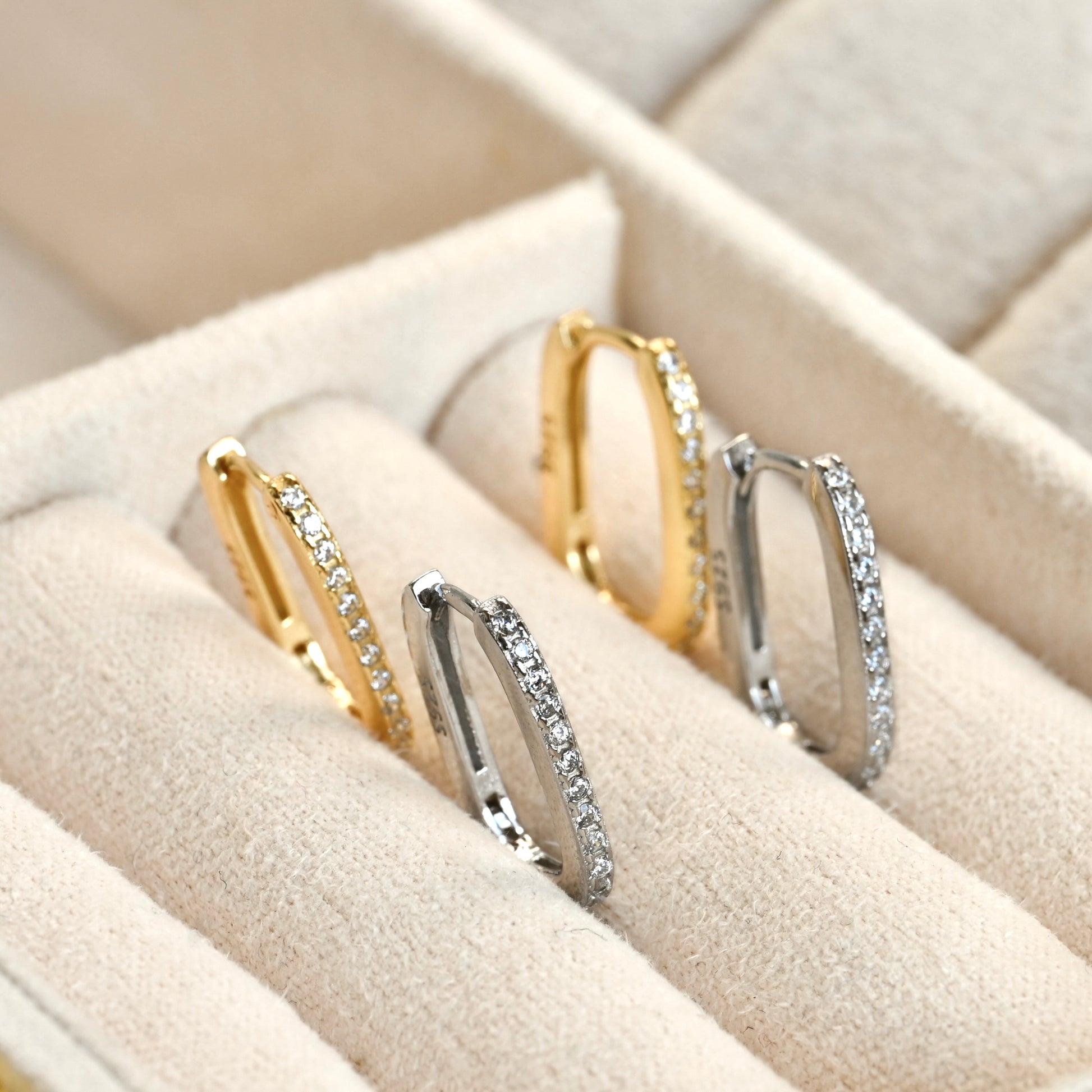 Pair of gold and silver hoop earrings  with CZ accents on a beige jewelry box.
