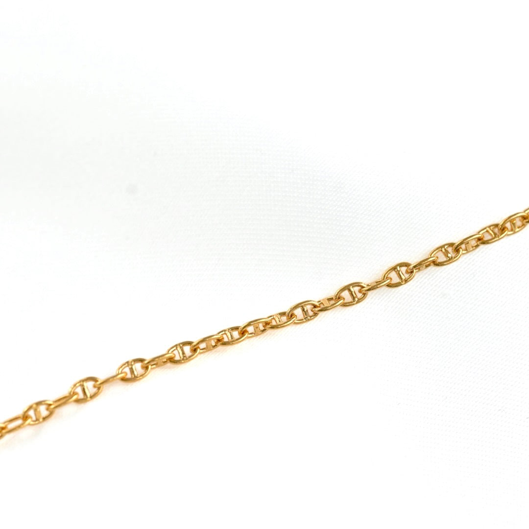 A close-up of a gold chain with oval links, laid diagonally across a white textured background.