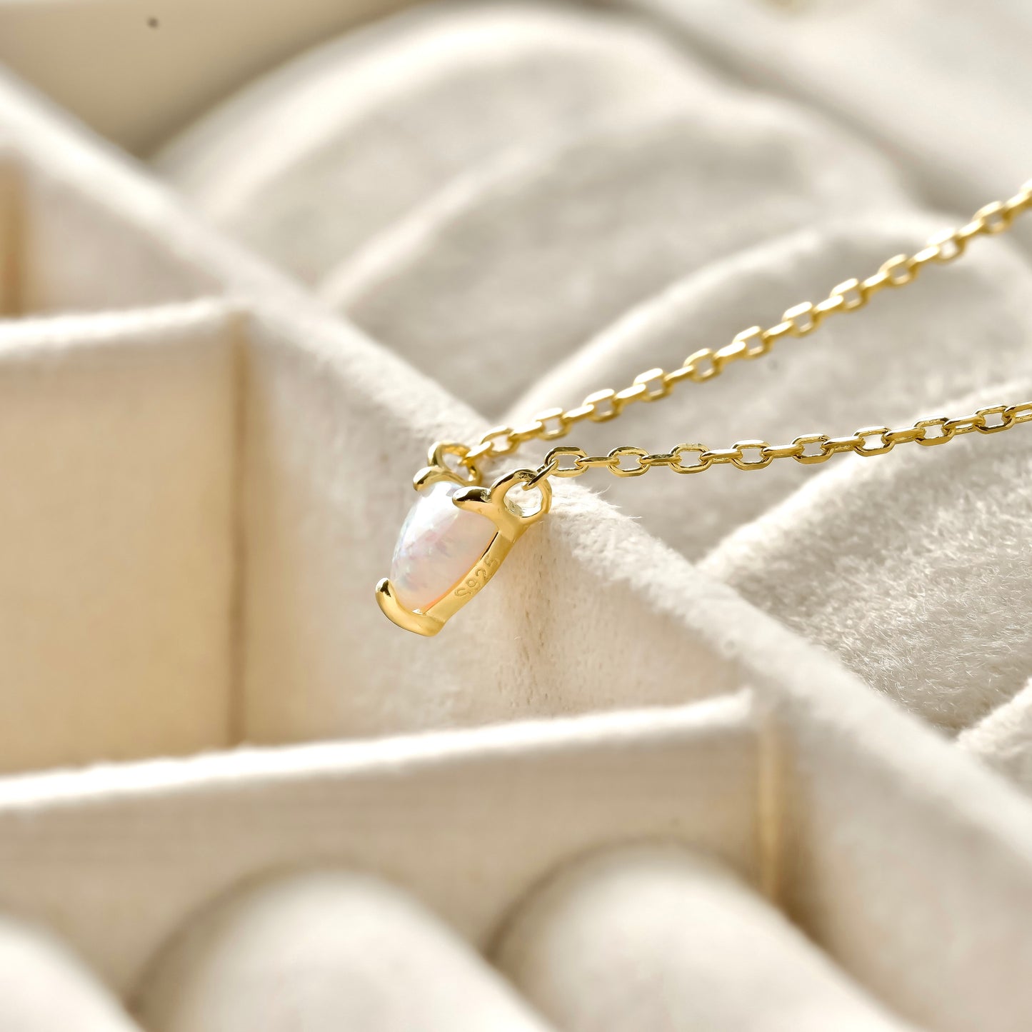 Side view of gold necklace with a heart charm on a textured beige surface
