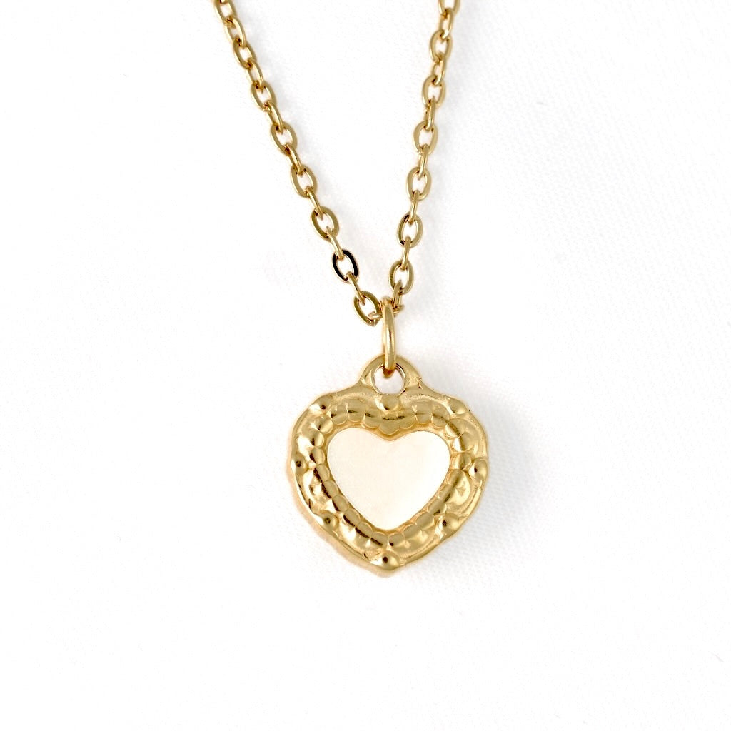 A gold heart pendant necklace with a textured outer border and a smooth, heart center with mother of pearl inlay, suspended from a delicate gold chain against a plain white background.