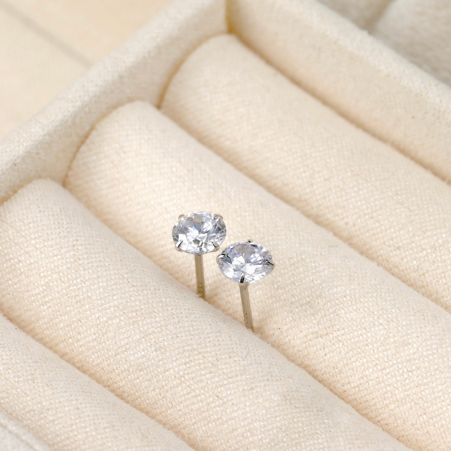 Pair of silver stud earrings on a soft beige ring tray.