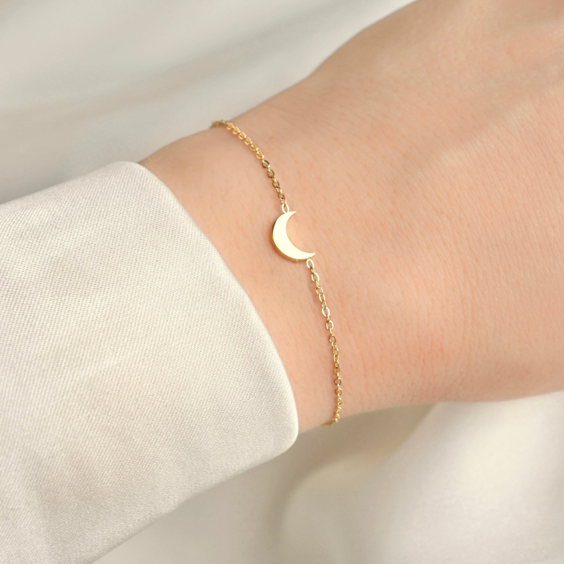 Gold bracelet with a dainty moon design on a wrist against a light background
