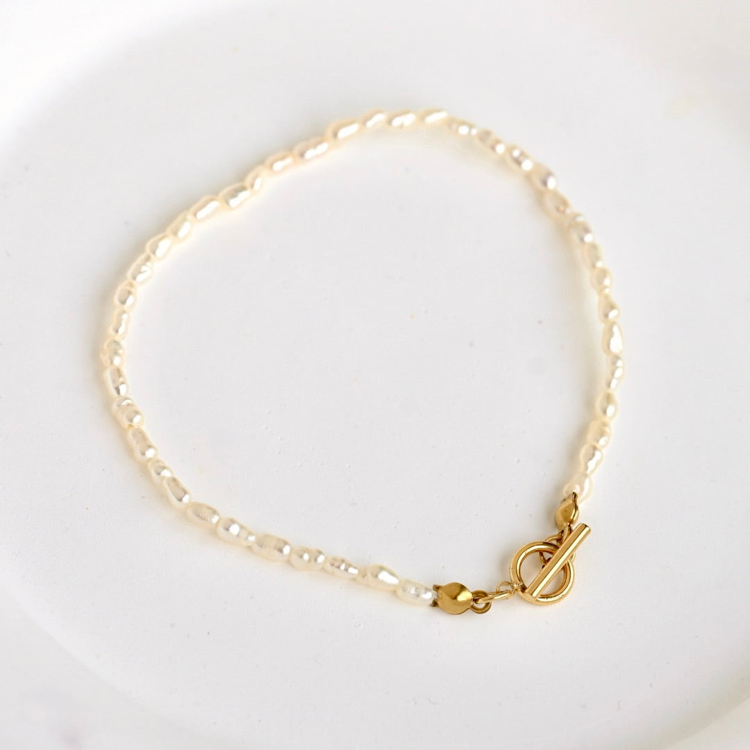 A delicate bracelet made of small white pearls linked with a gold clasp, photographed on a clean white background.