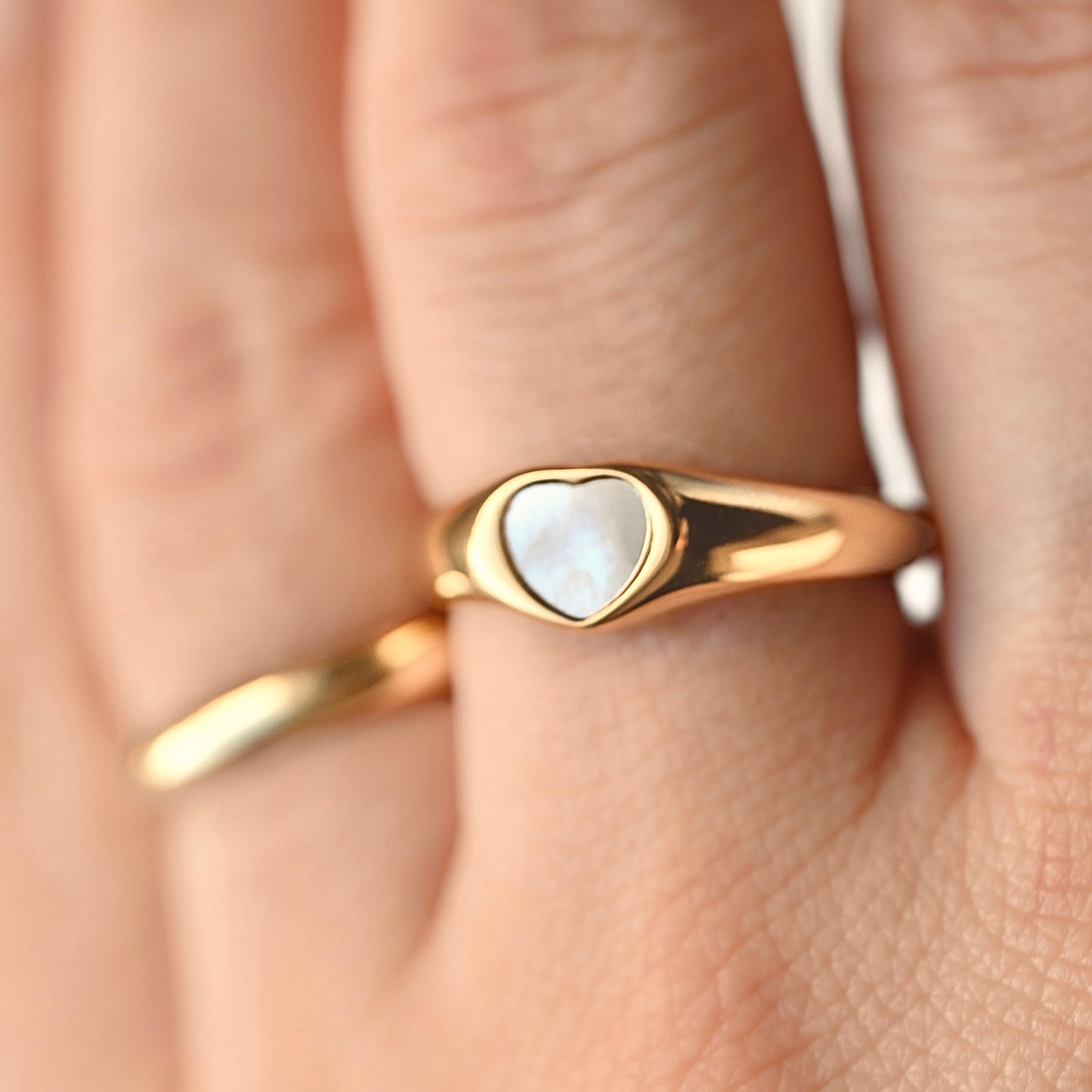 Gold heart ring with a shell inlay on a finger