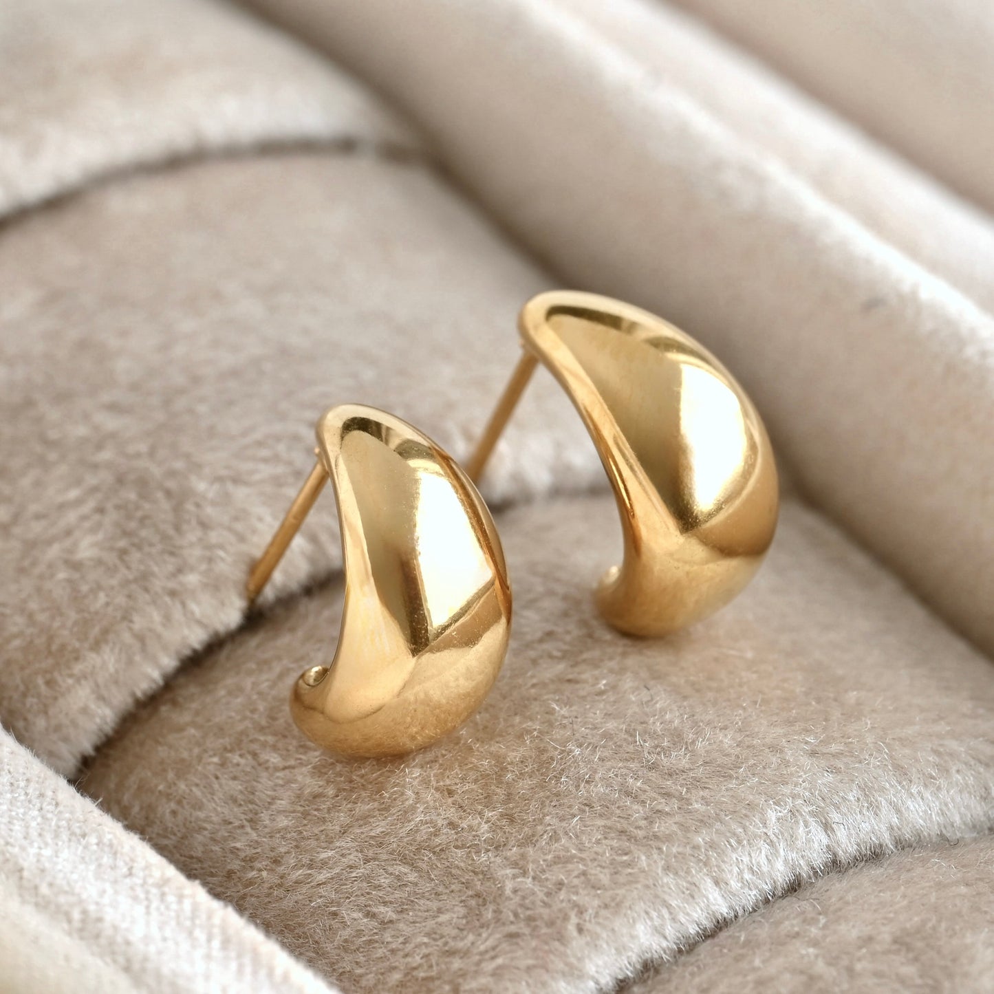 Thick gold dome earrings on a soft beige fabric background