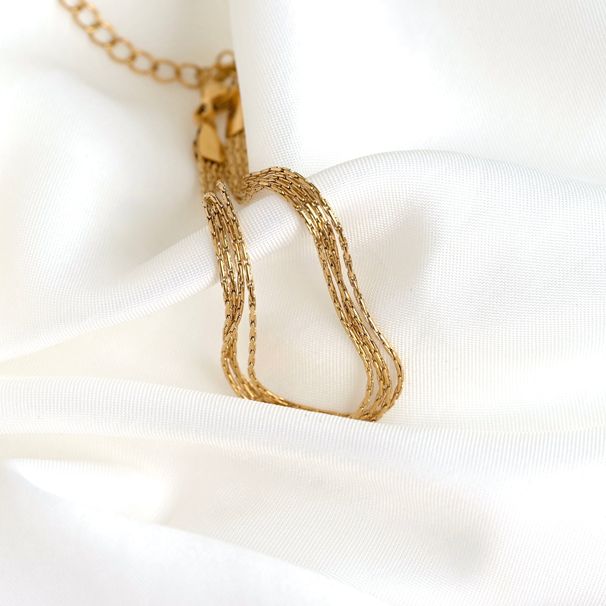A close-up of a gold-toned multi-strand chain bracelet draped over soft white satin fabric.