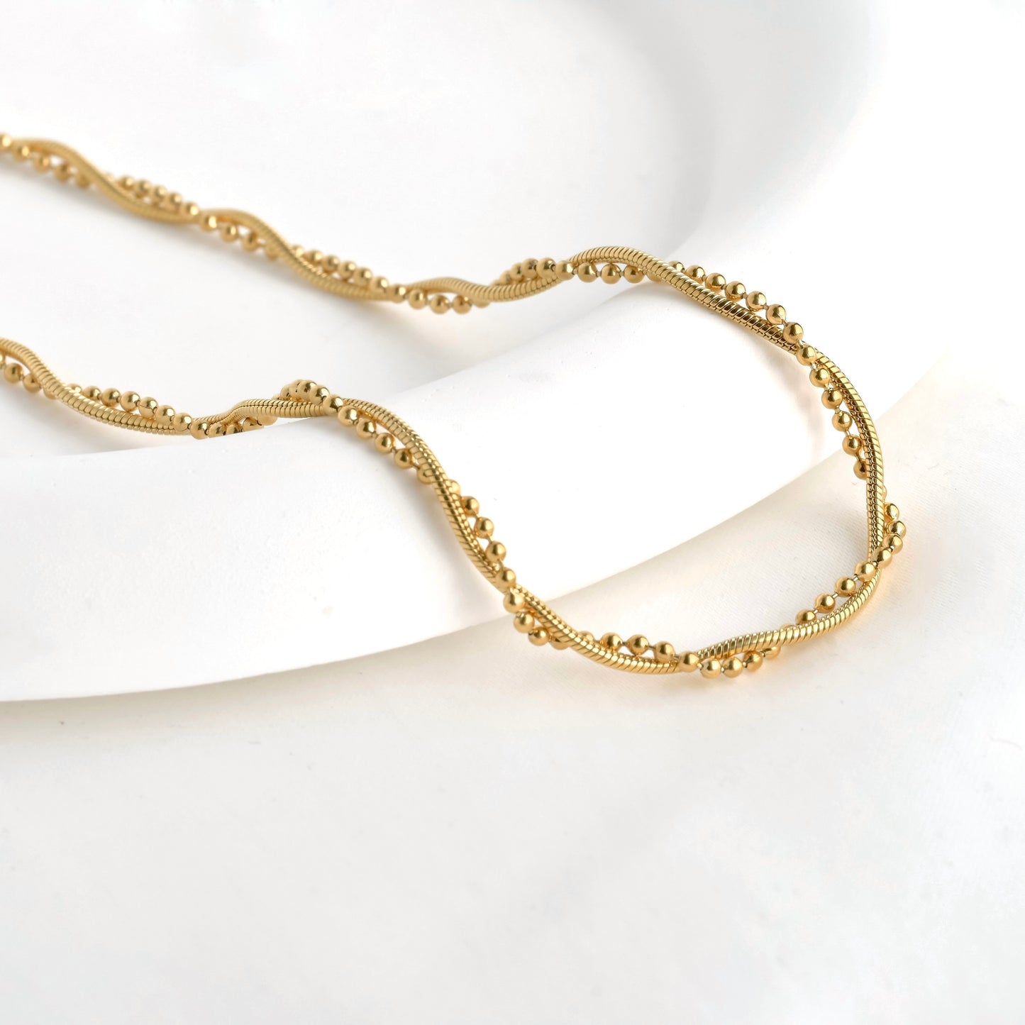 Twisted snake chain and ball chain necklace in gold on a white background