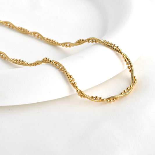 Twisted snake chain and ball chain necklace in gold on a white background