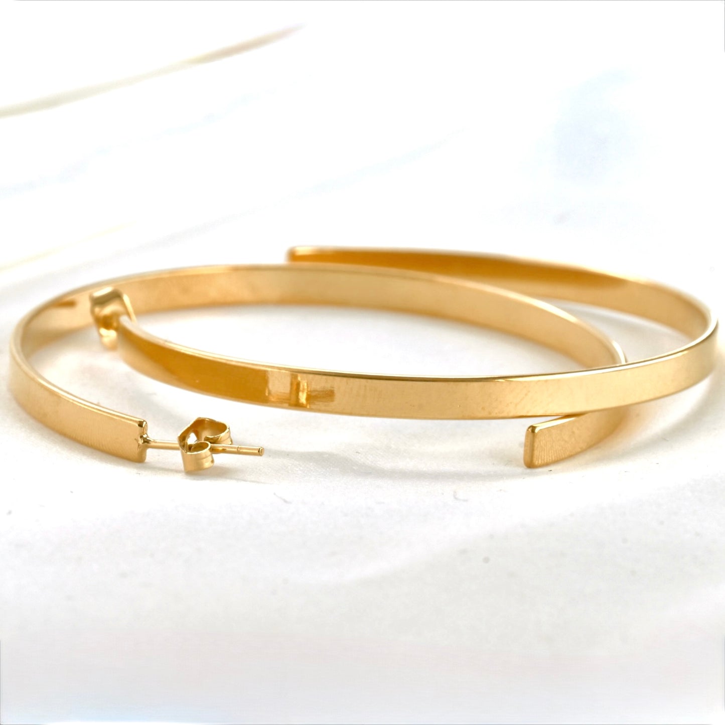 Gold oversized hoop studs stacked on a white background