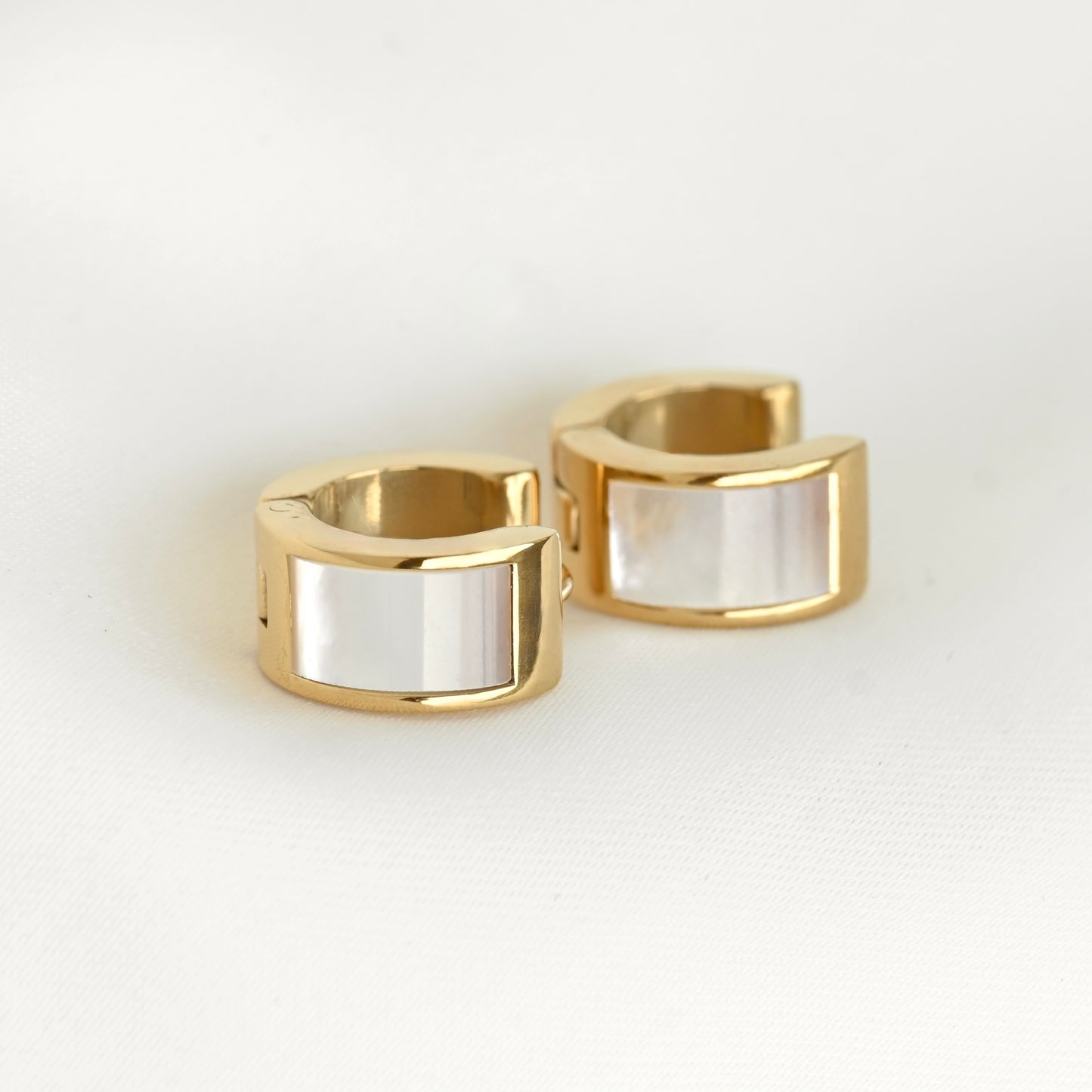 A pair of gold-plated huggie hoop earrings with a smooth, polished white shell inlay, displayed on a clean white surface.