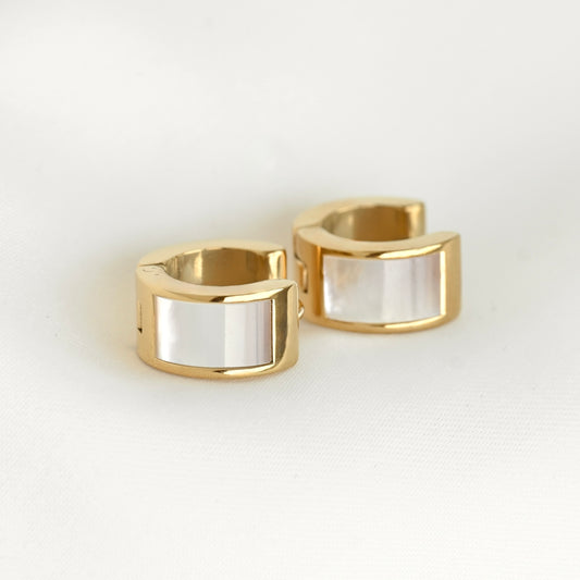 A pair of gold-plated huggie hoop earrings with a smooth, polished white shell inlay, displayed on a clean white surface.