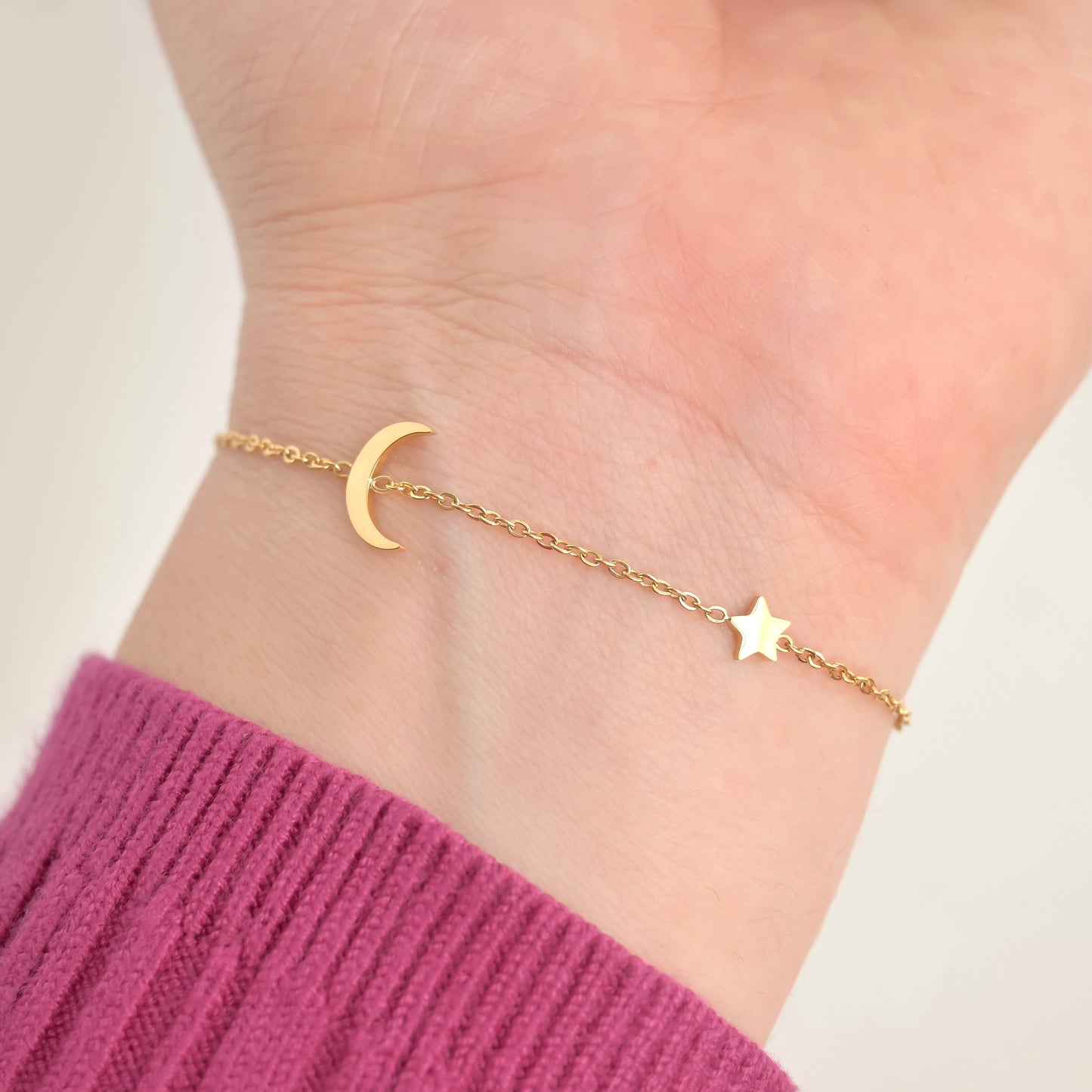 Gold bracelet with moon and star charms on a wrist against a light background