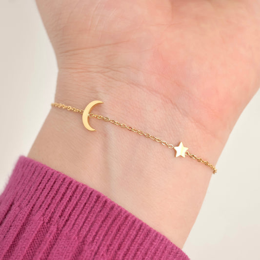Gold bracelet with moon and star charms on a wrist against a light background