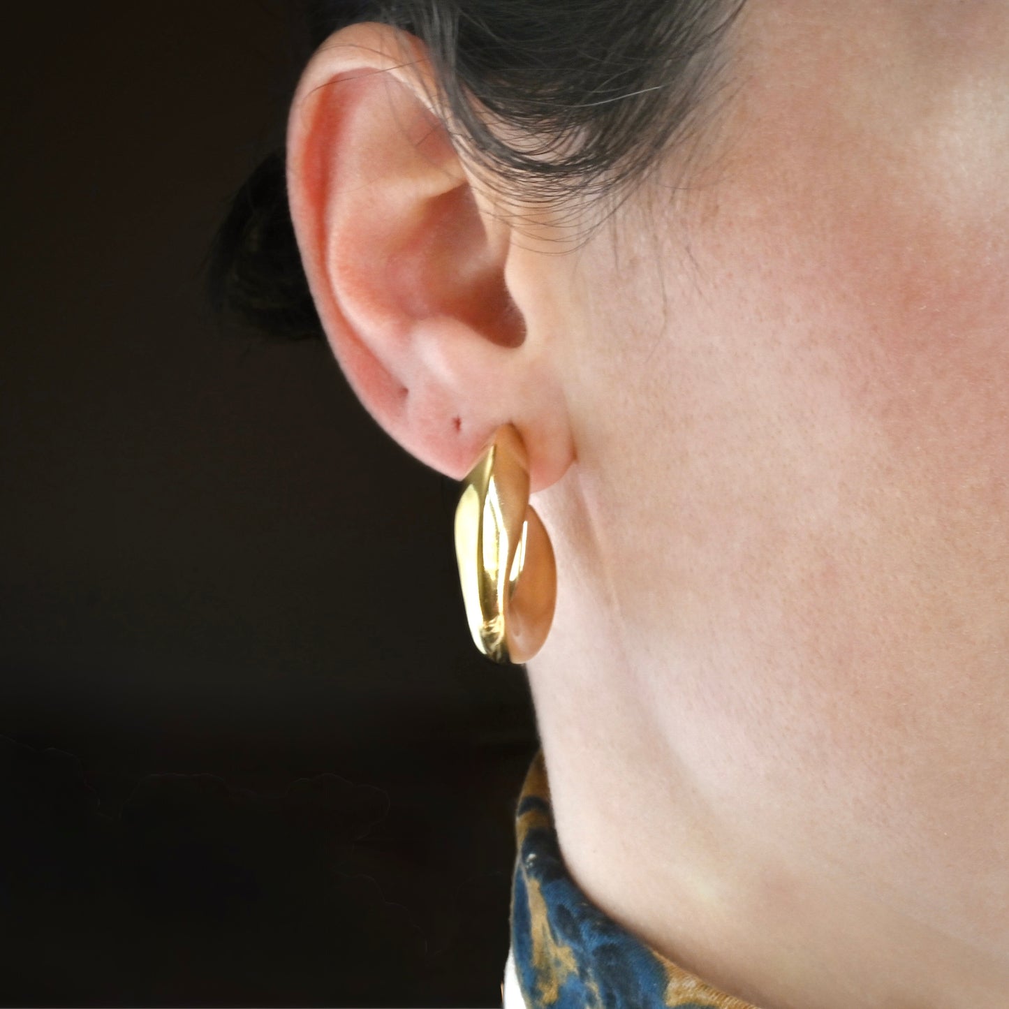 Front view of gold hoop earrings worn by a person against a dark background