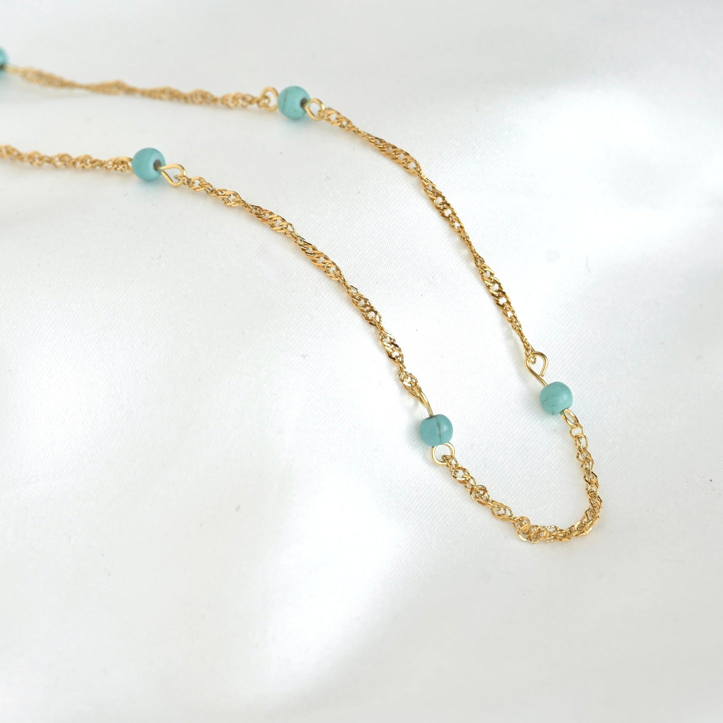 A delicate gold chain necklace featuring small, round light blue-green beads spaced along the chain, displayed on a clean white background.