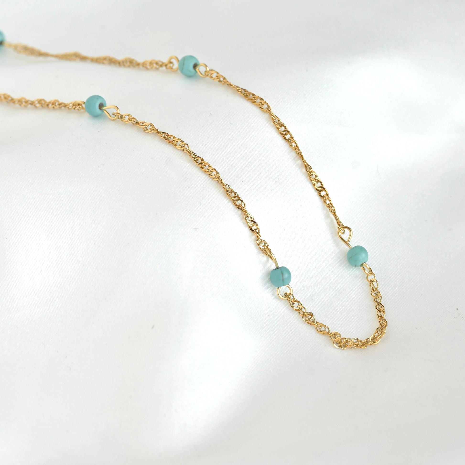 A delicate gold chain necklace featuring small, round light blue-green beads spaced along the chain, displayed on a clean white background.