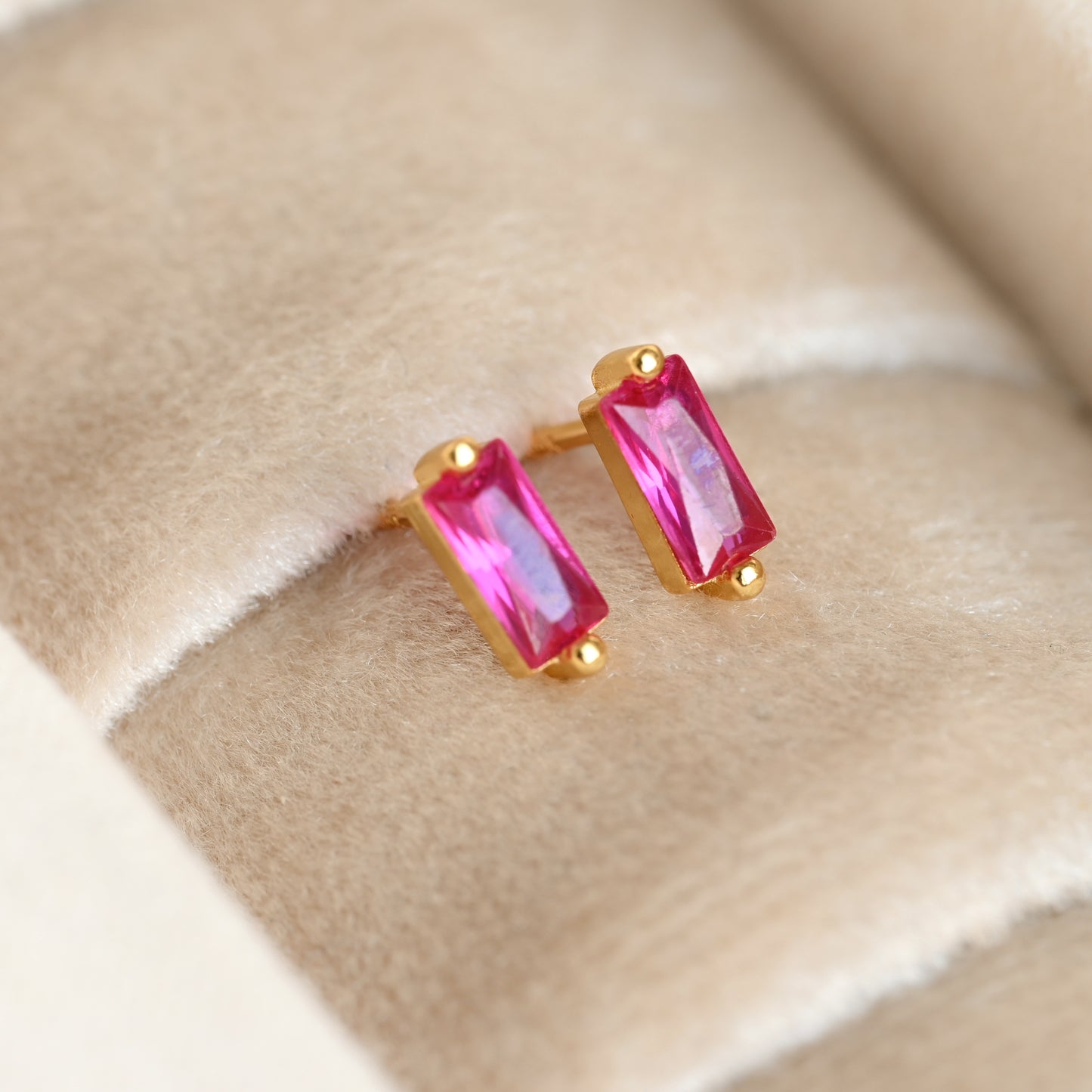 Gold earrings with pink gemstones on a beige fabric background