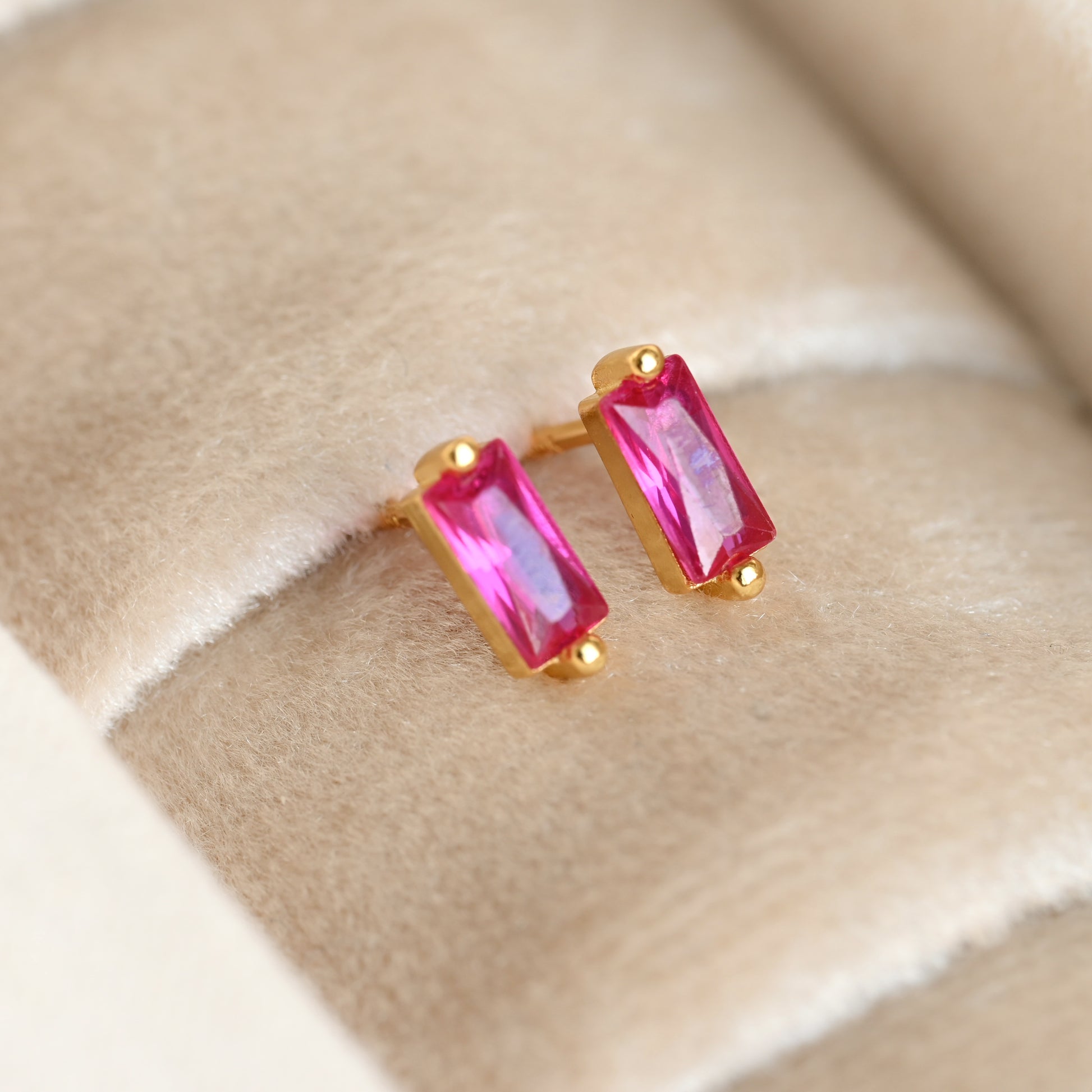 Gold earrings with pink gemstones on a beige fabric background