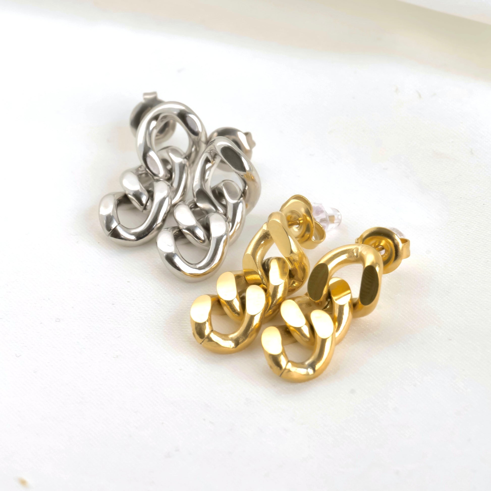 Pair of cuban link chain earrings in gold and silver on a white background