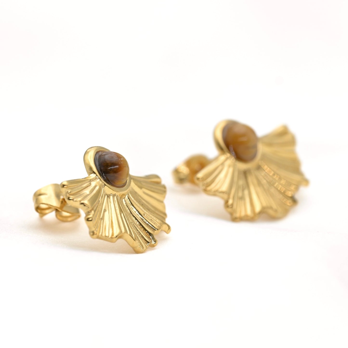 Pair of organic shapoed fan earrings with brown stone resting against white fabric