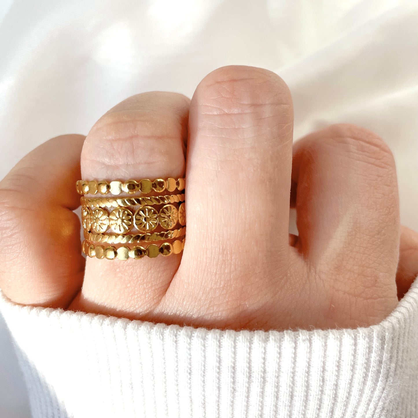 Boho layered gold ring on a finger against a white background