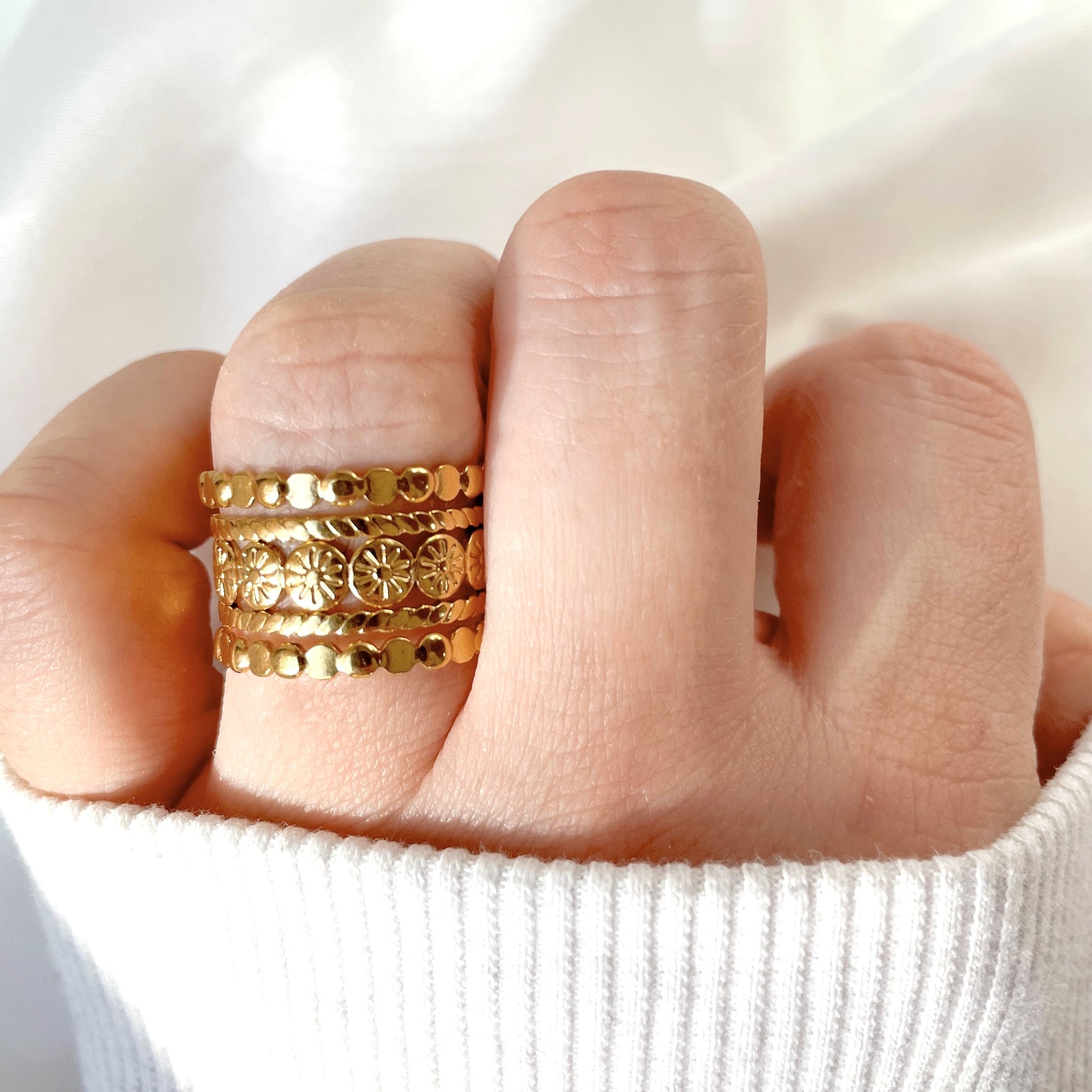Boho layered gold ring on a finger against a white background