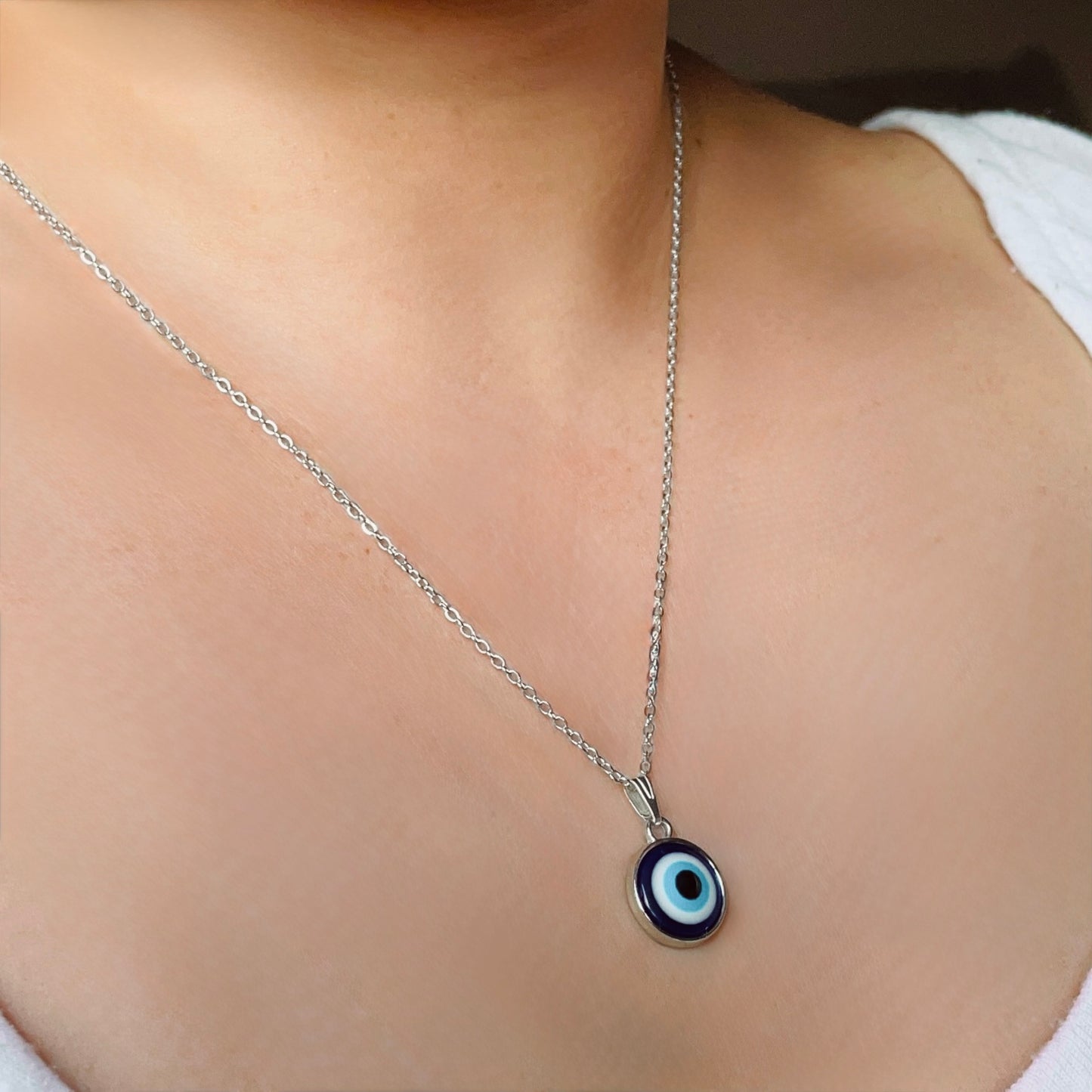 Silver necklace with a blue and white evil eye pendant on a woman wearing a white top.