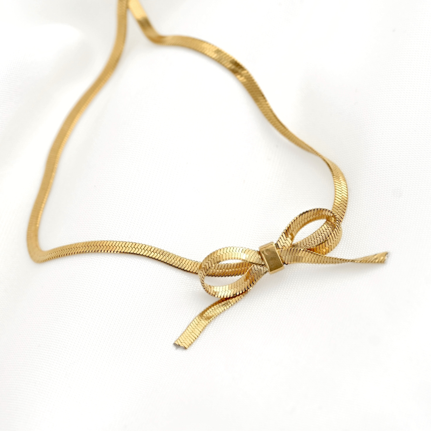 Angled front view of Aagold-tone snake chain necklace with a decorative bow knot at the center, displayed on a clean white background.