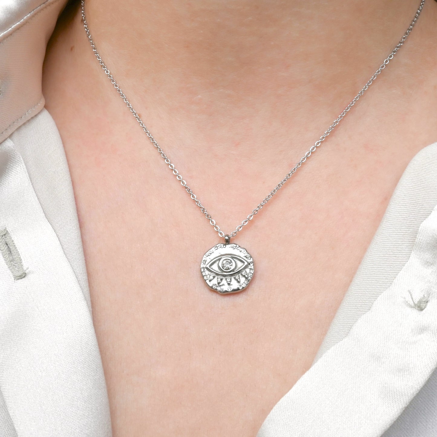 Silver necklace with an eye pendant worn by a person in a white outfit.