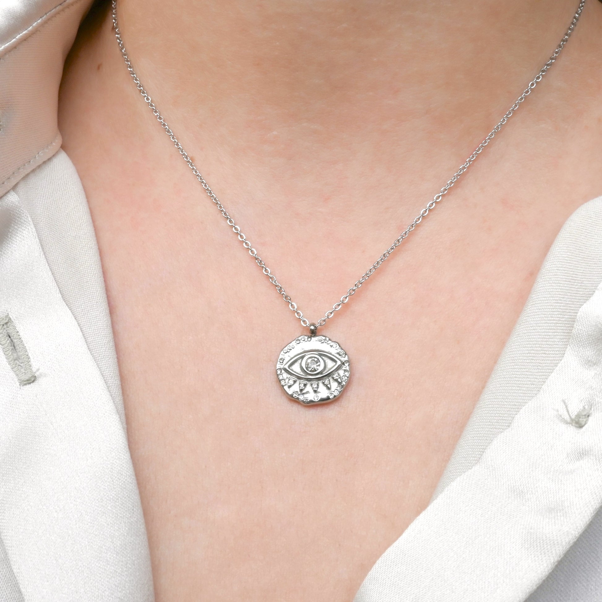 Silver necklace with an eye pendant worn by a person in a white outfit.