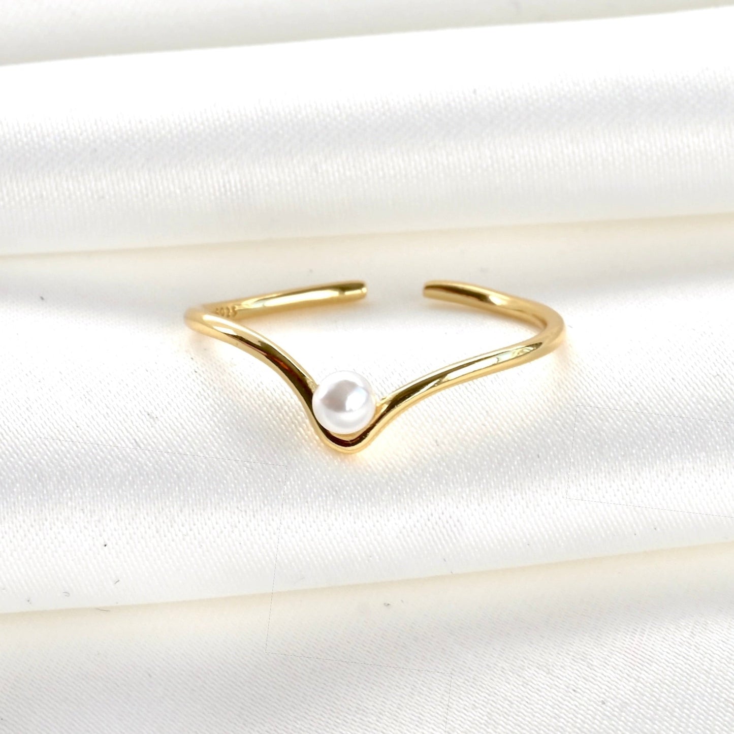 Adjustable gold wishone ring with a pearl on a white fabric background