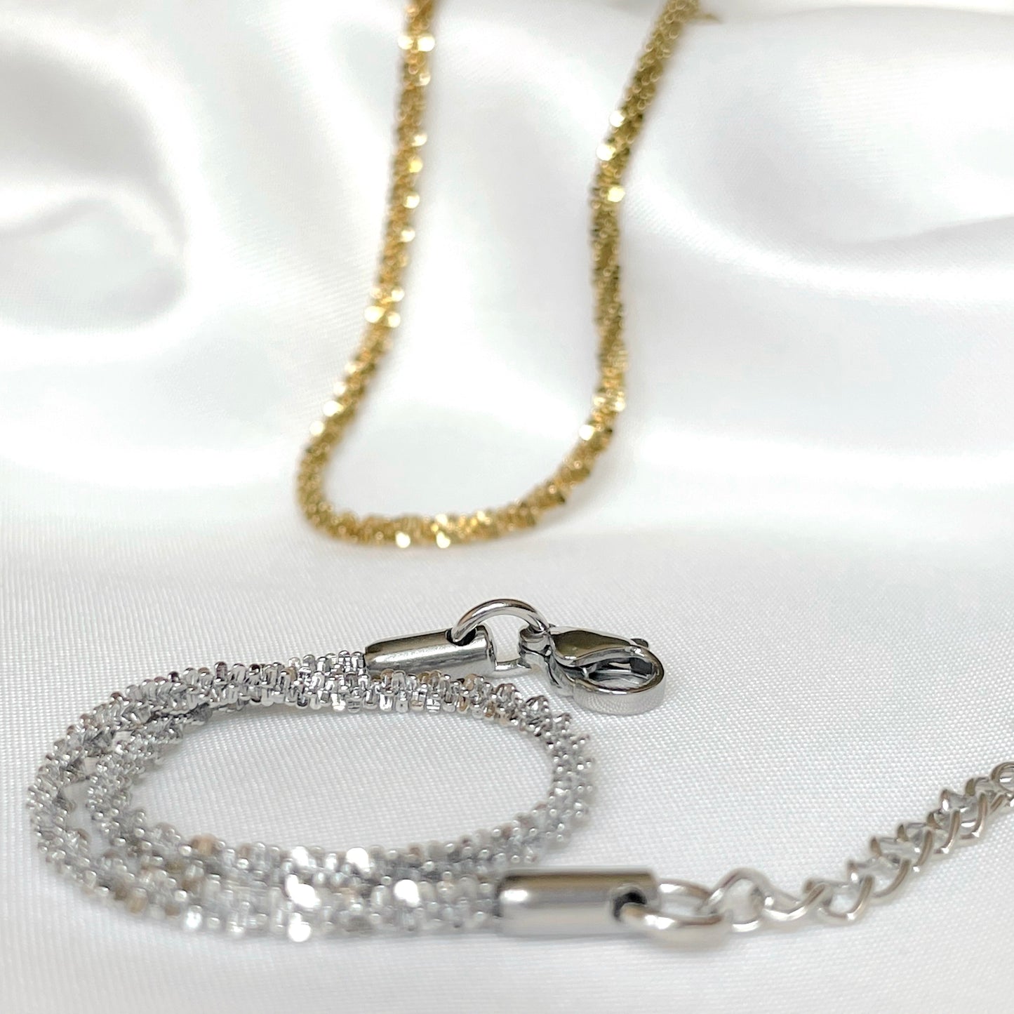 Sparkling chain bracelets in gold and silver on a white satin background