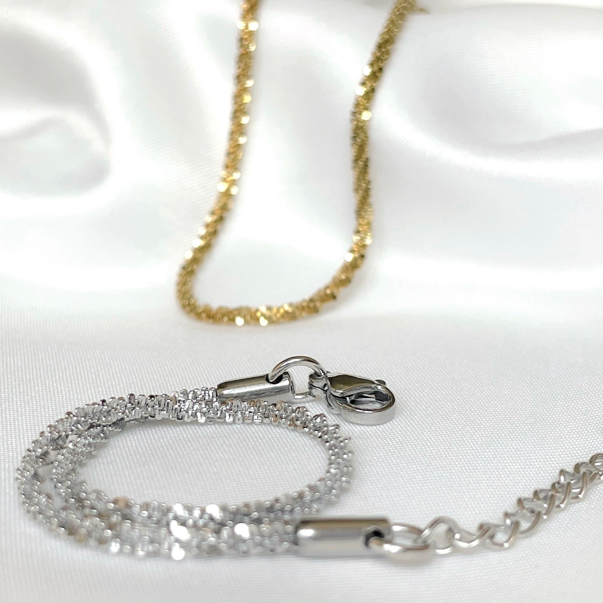 Sparkling chain bracelets in gold and silver on a white satin background