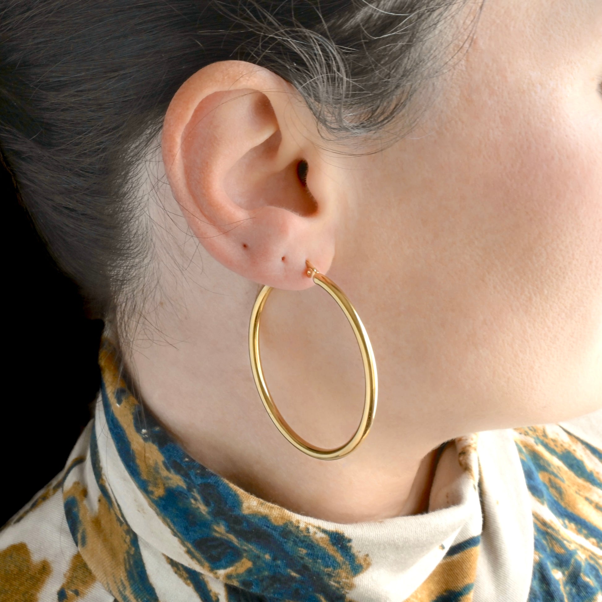 50mm gold tunnel hoop earrings worn by a person with a patterned garment.
