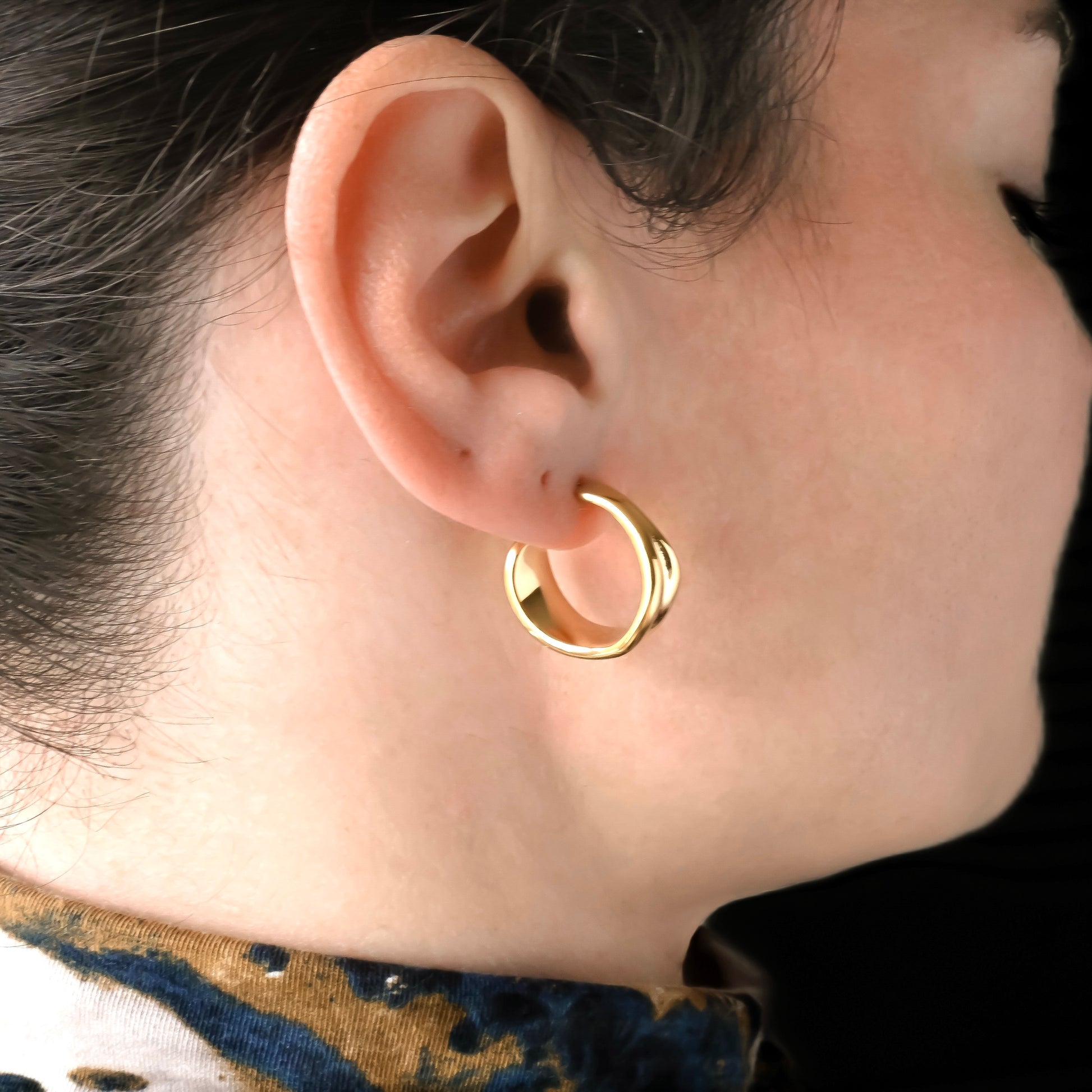 Close-up of an ear wearing wide organic gold hoop earrings