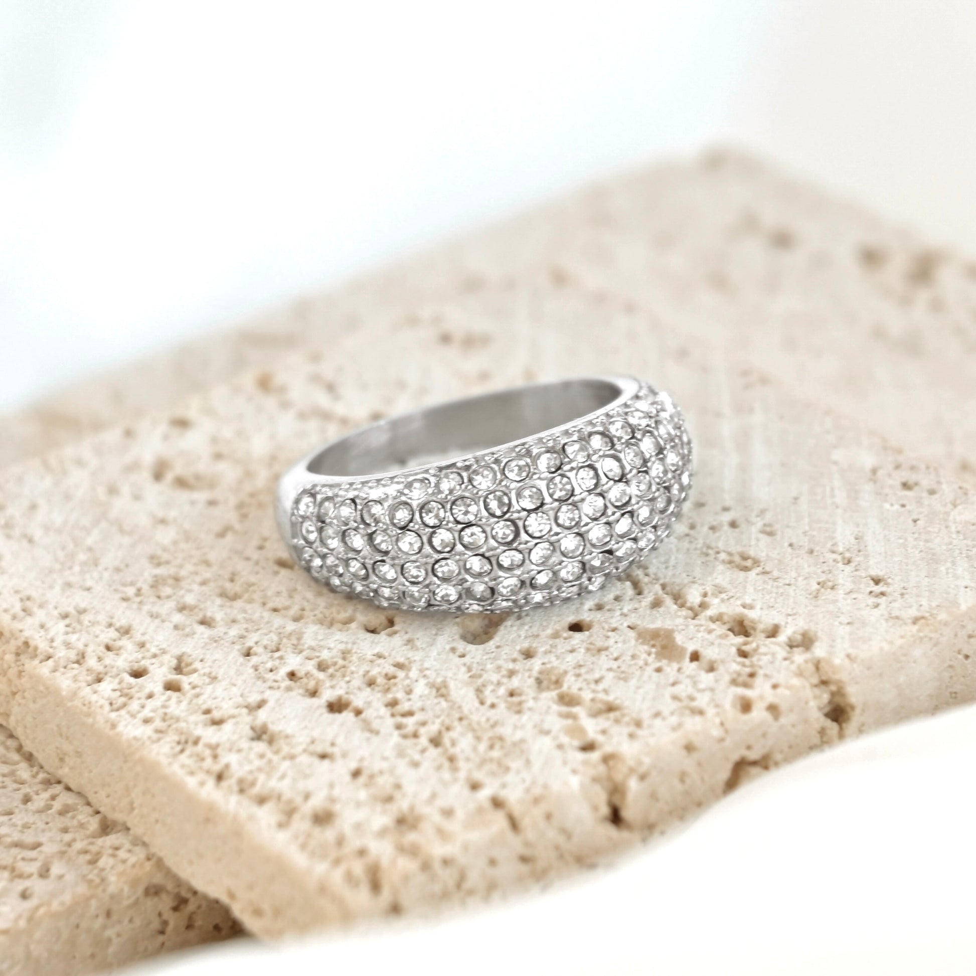 Silver ring with embedded stones on a textured beige surface