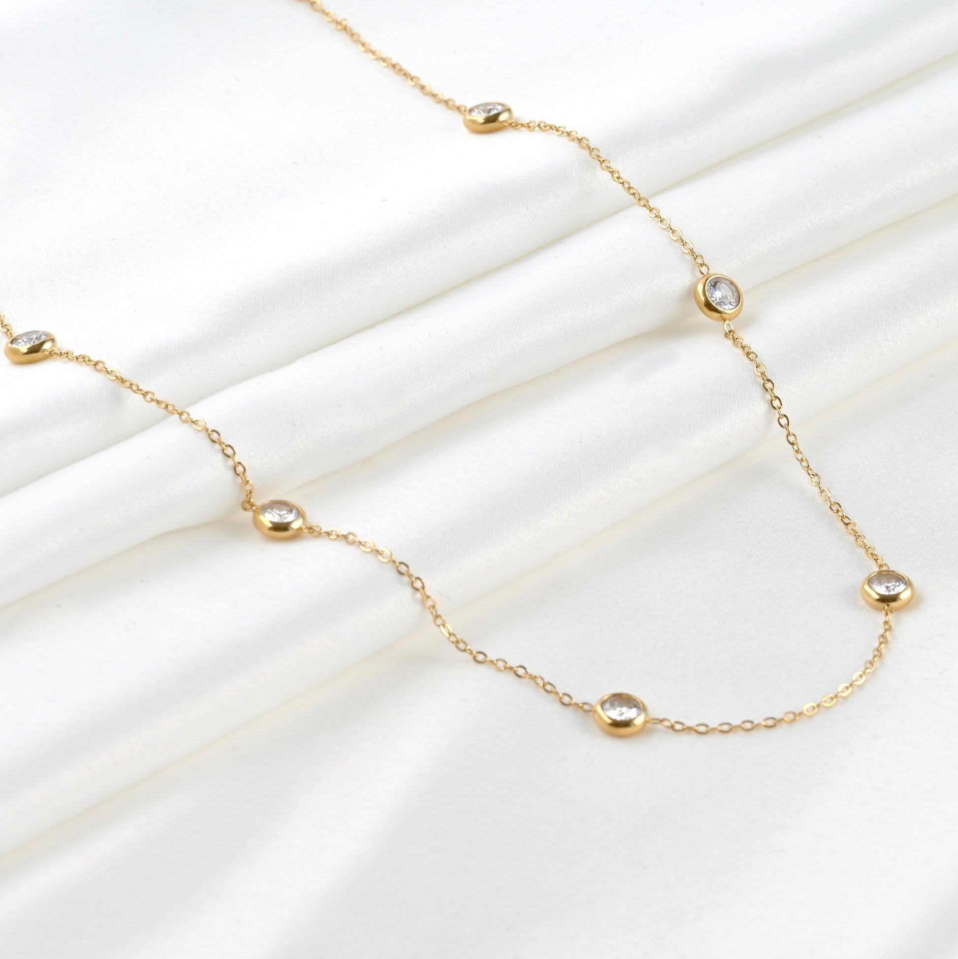 Wide angles view of gold bezel set necklace with small crystal accents on folded white satin