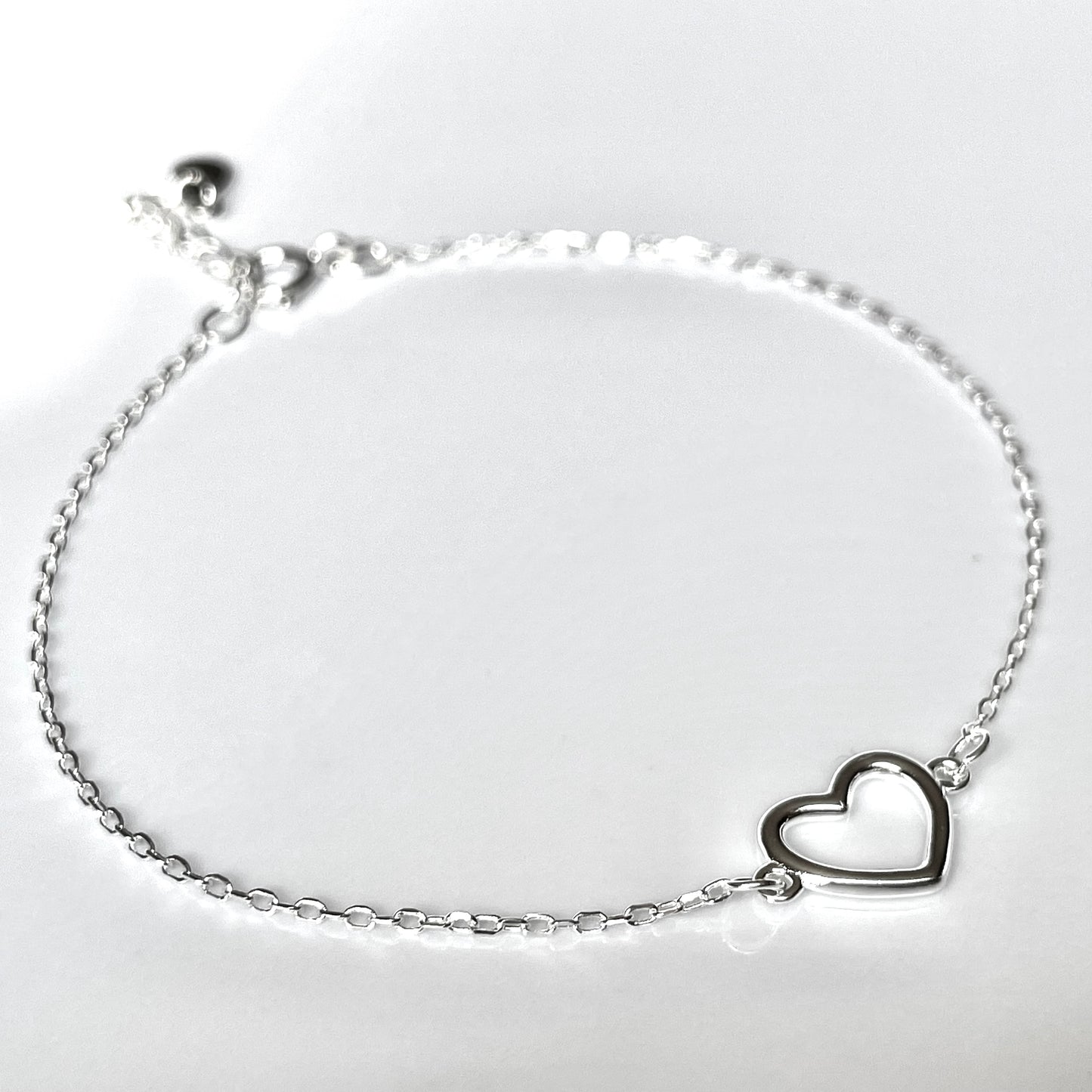 Close-up view of silver bracelet with a heart charm on a light gray background