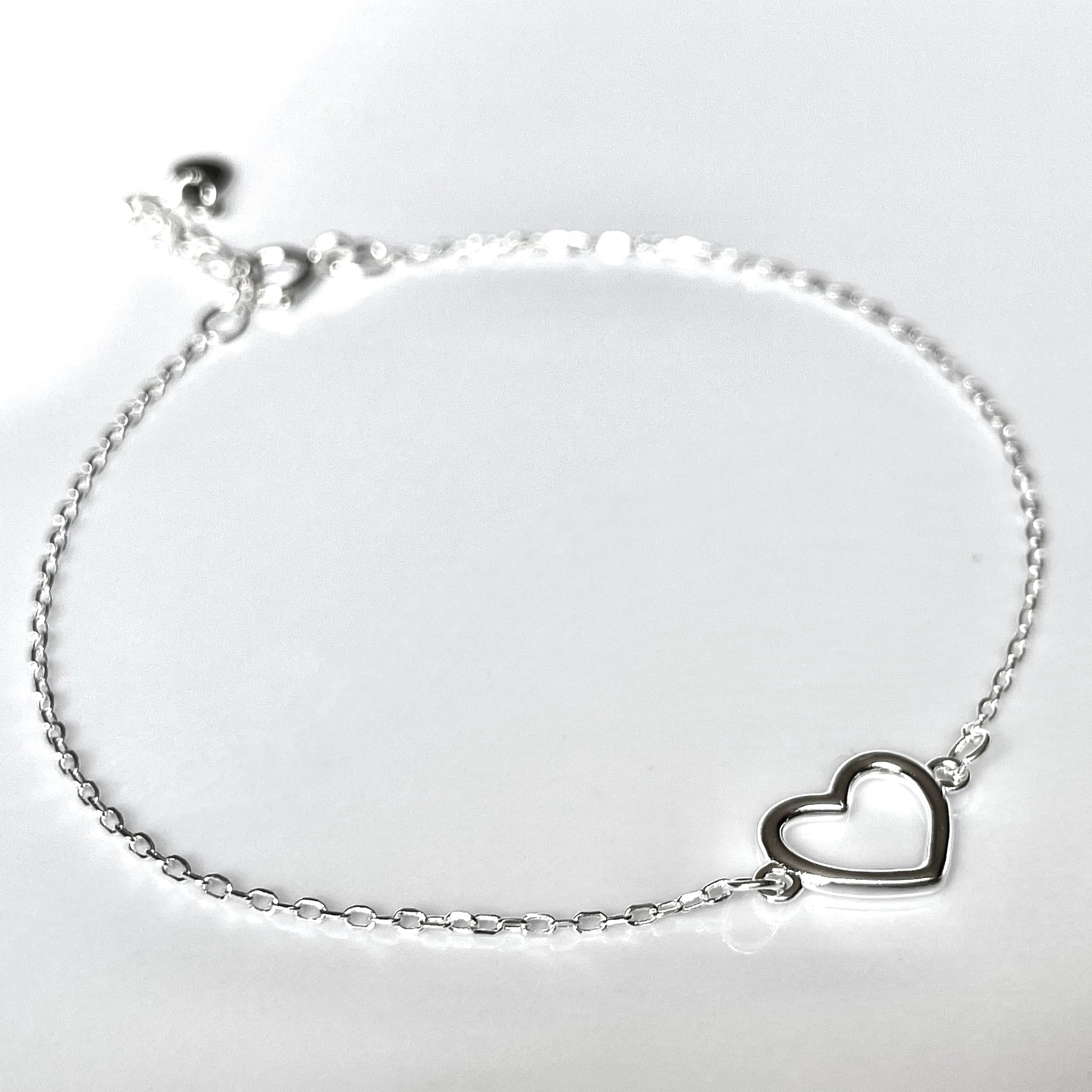 Close-up view of silver bracelet with a heart charm on a light gray background