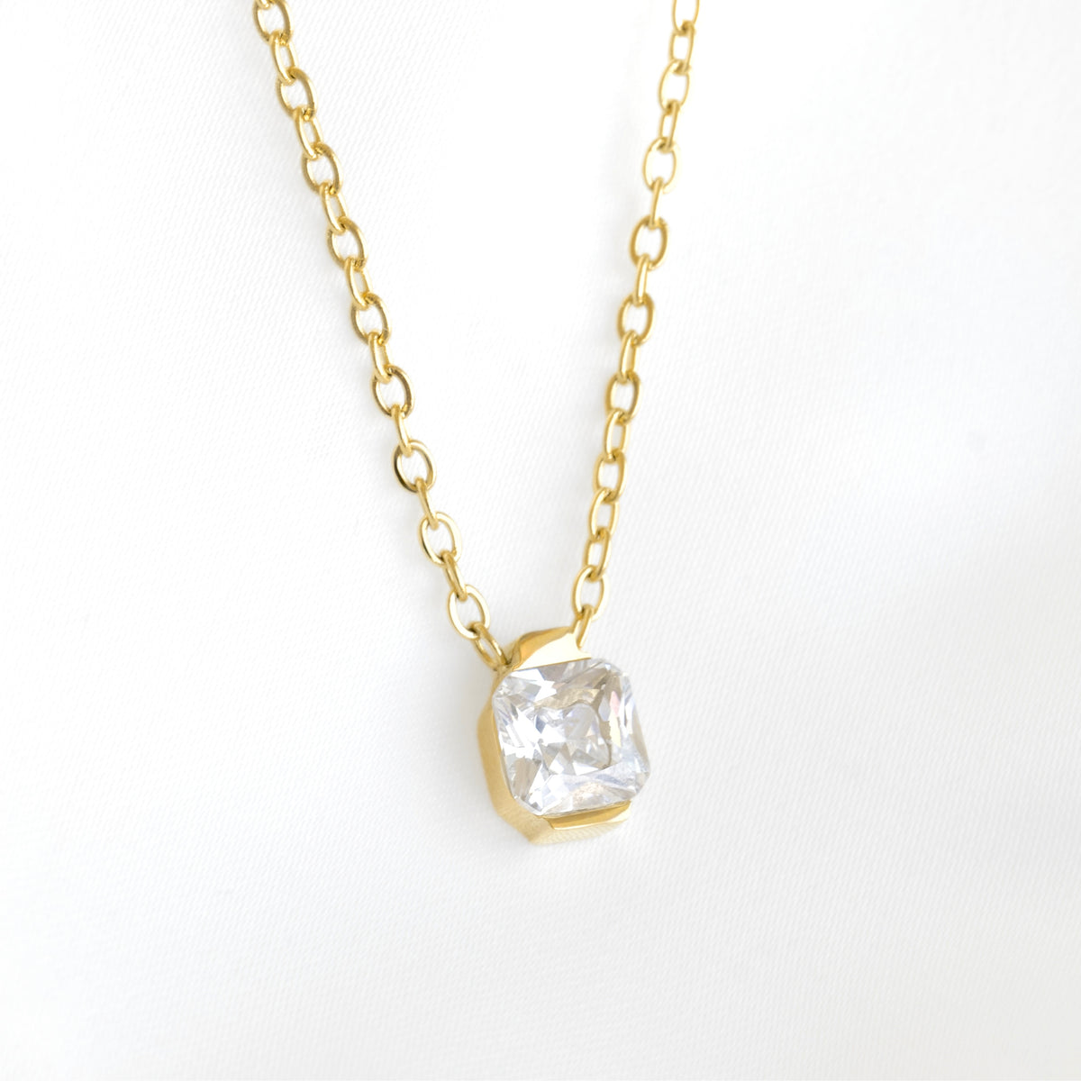 A delicate gold chain necklace with a cushion-cut clear gemstone pendant in a gold bezel setting, displayed on a clean white background.