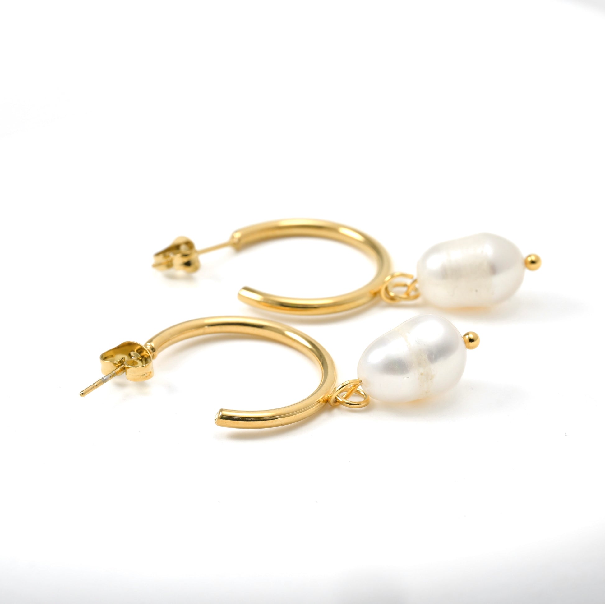 Dainty gold hoop earrings with white oval pearls on a white background