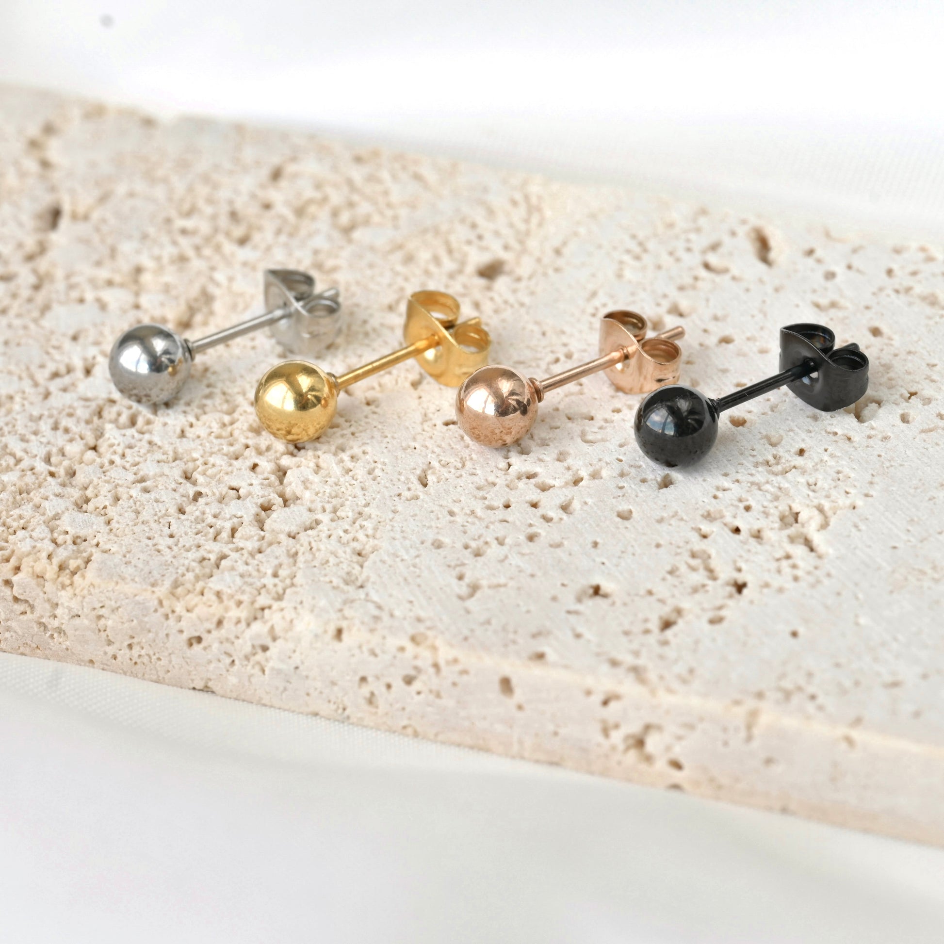 Set of four pairs of sphere stud earrings in silver, gold, rose gold, and black on a textured surface.