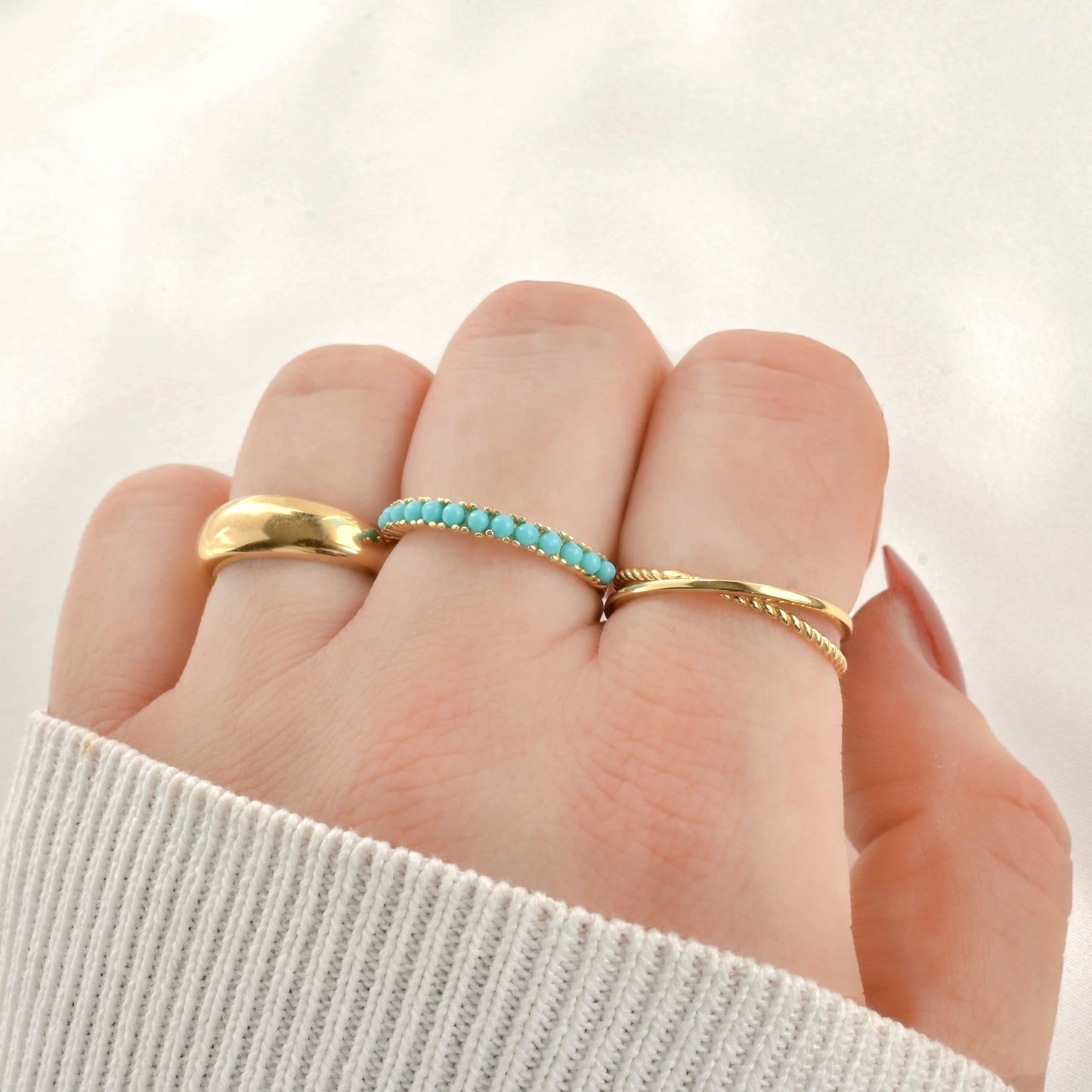 Three gold rings stacked on a hand inclusing criss cross ring with interlocking bands, turquoise gemstone ring and chunky dome ring