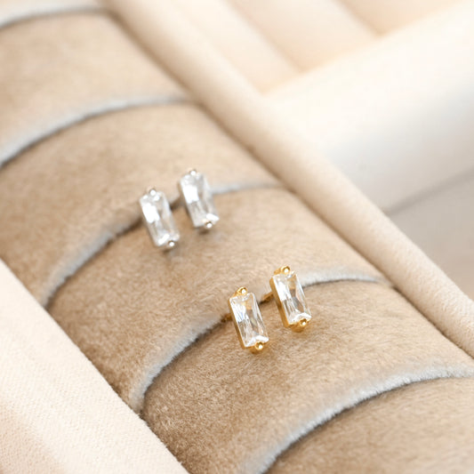 Gold bar earrings with clear stones on a beige jewelry display