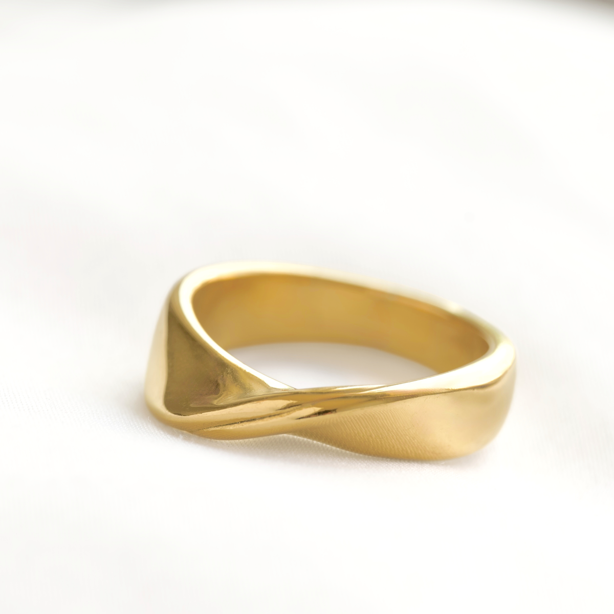 A polished yellow gold ring with a twisted, fluid design, resting on a clean white surface.